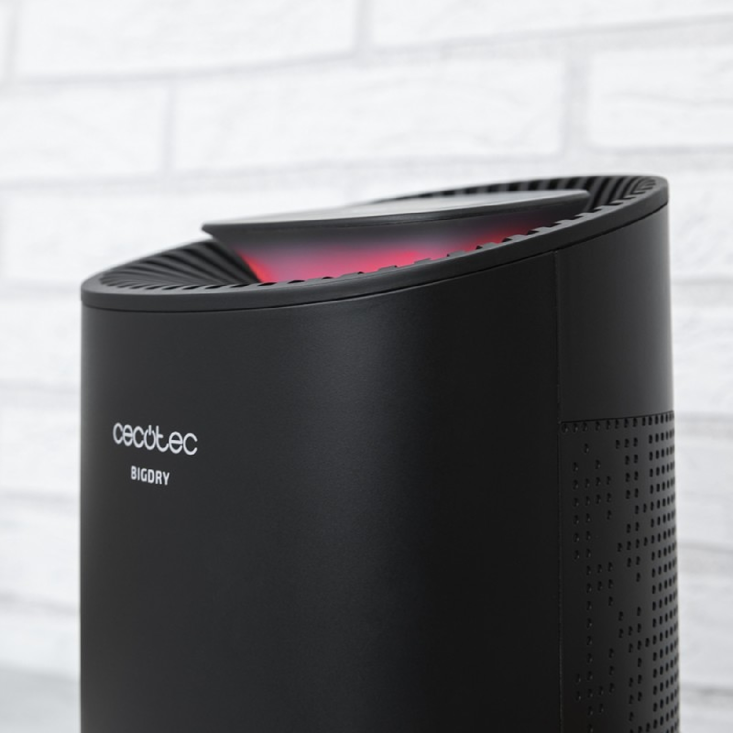 Czarny oczyszczacz powietrza z czerwonym światłem na górze, na tle białej ceglanej ściany.