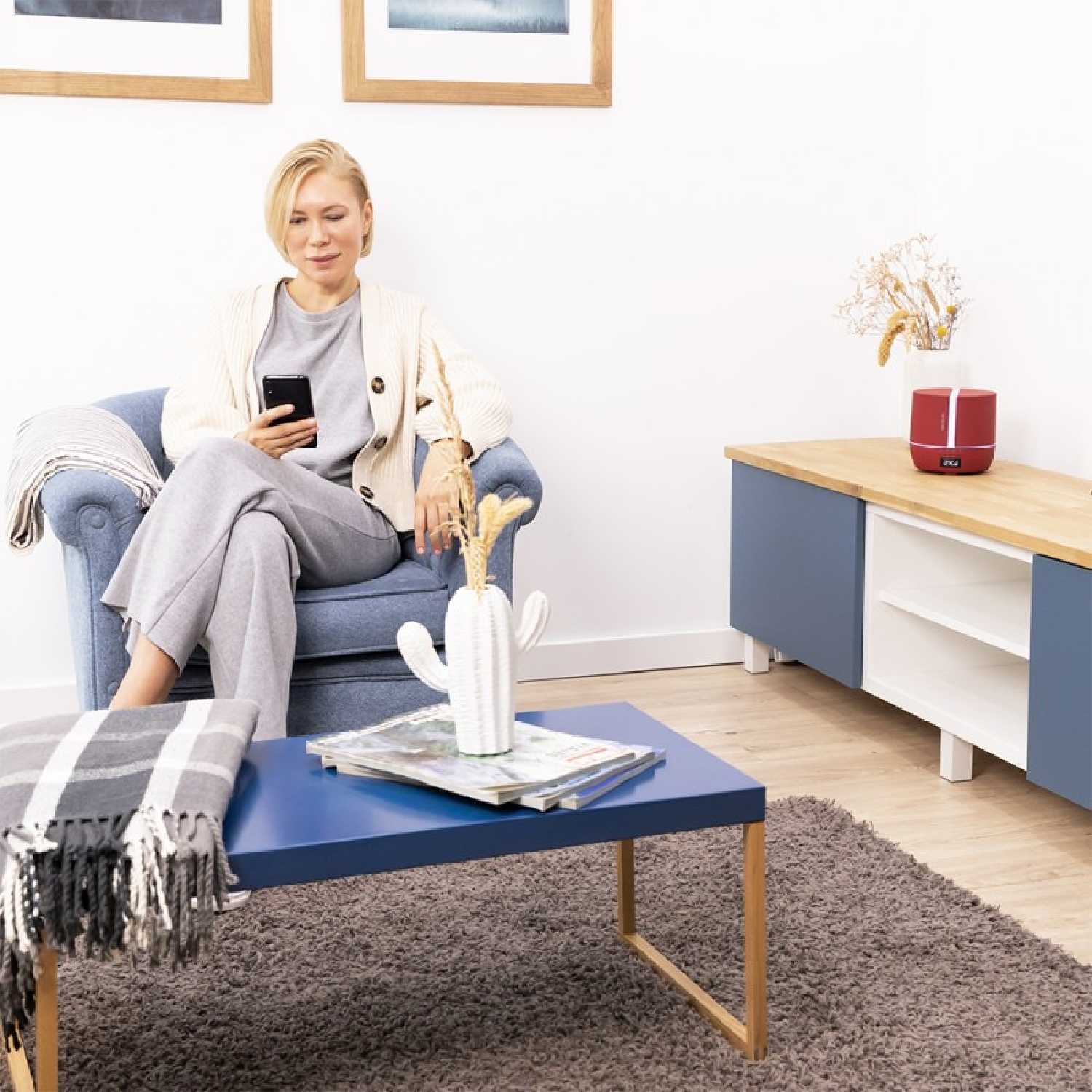 Frau in einem Raum sitzt in einem Stuhl. Sie hält ein Telefon. Es gibt einen kleinen Tisch und einen Schrank.