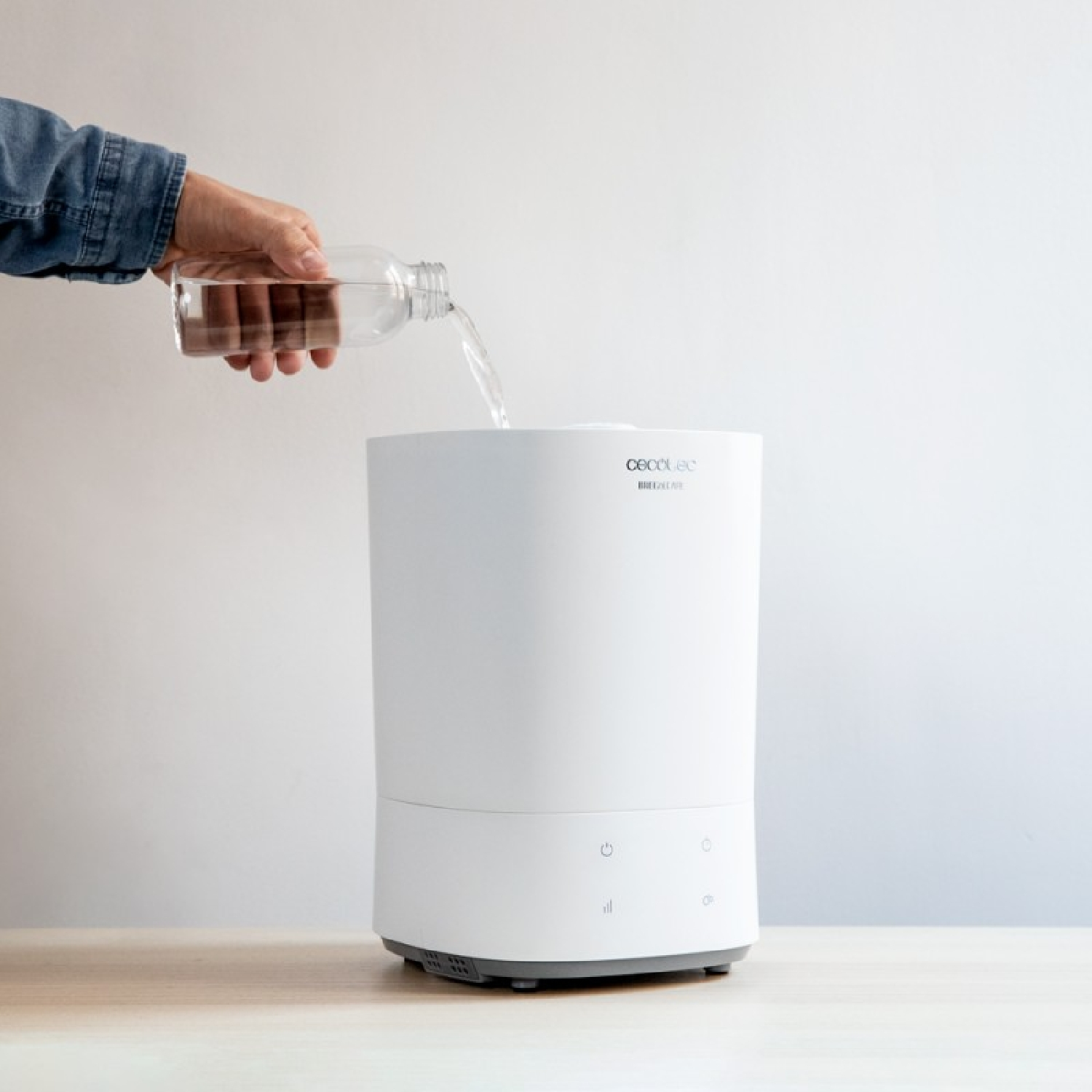 Persona che versa acqua in un umidificatore bianco su una superficie di legno, sfondo bianco.