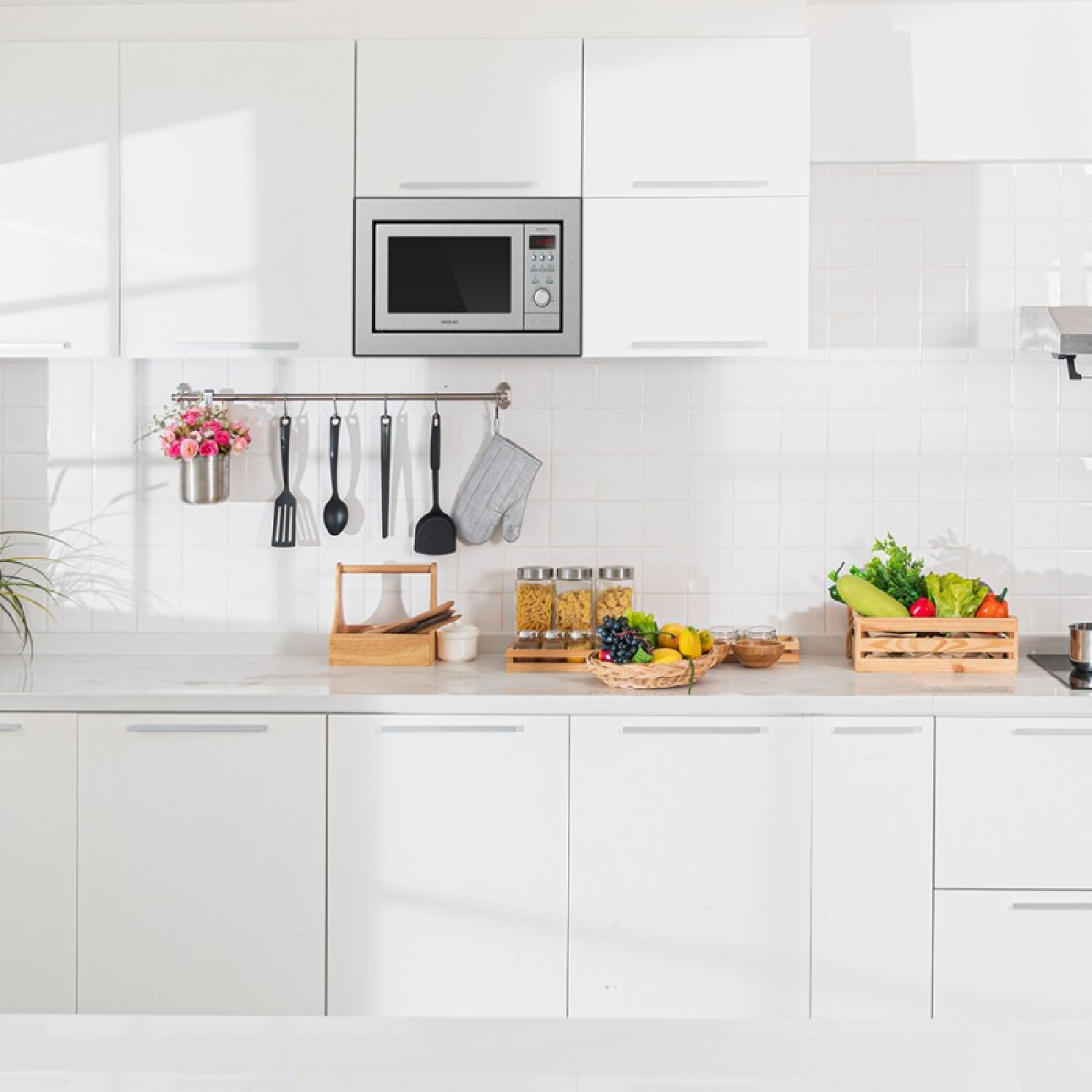 Biała kuchnia z kuchenką mikrofalową, szafkami i różnymi przedmiotami na blacie, w tym jedzeniem.