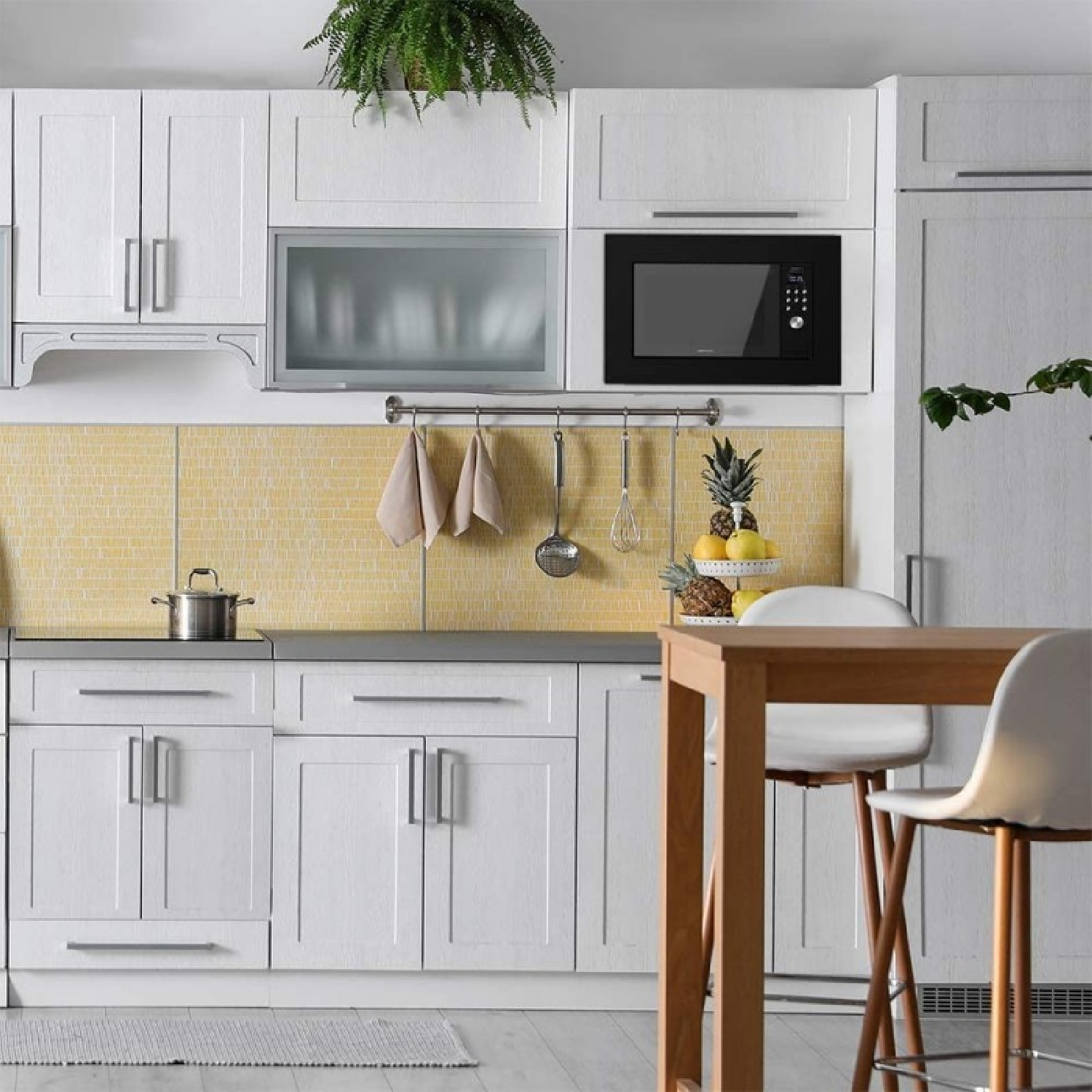Biała kuchnia z szafkami, kuchenką mikrofalową i żółtą glazurą. Stół z krzesłami na pierwszym planie.