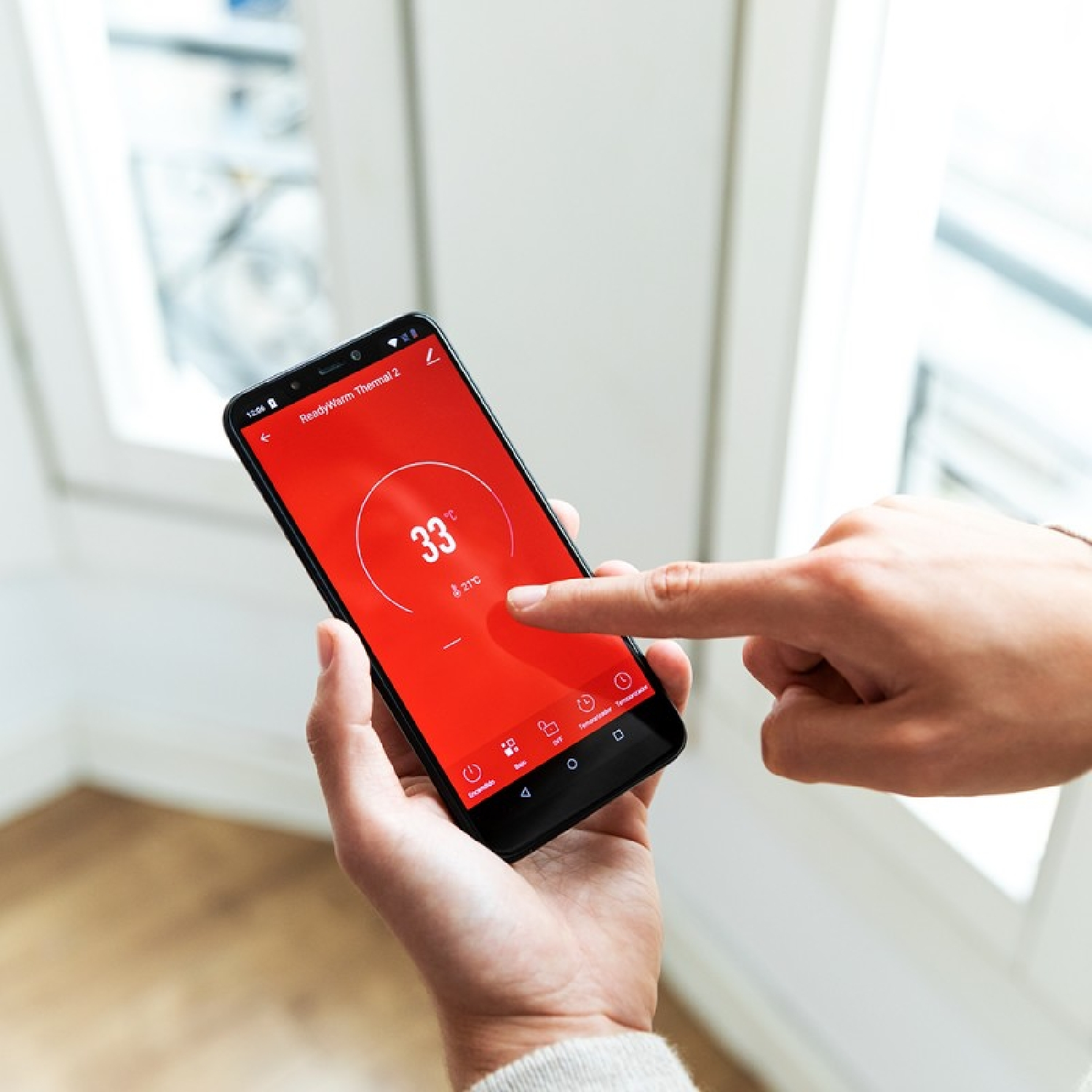 Osoba wskazująca na telefon wyświetlający temperaturę 33 stopni. Czerwony ekran.