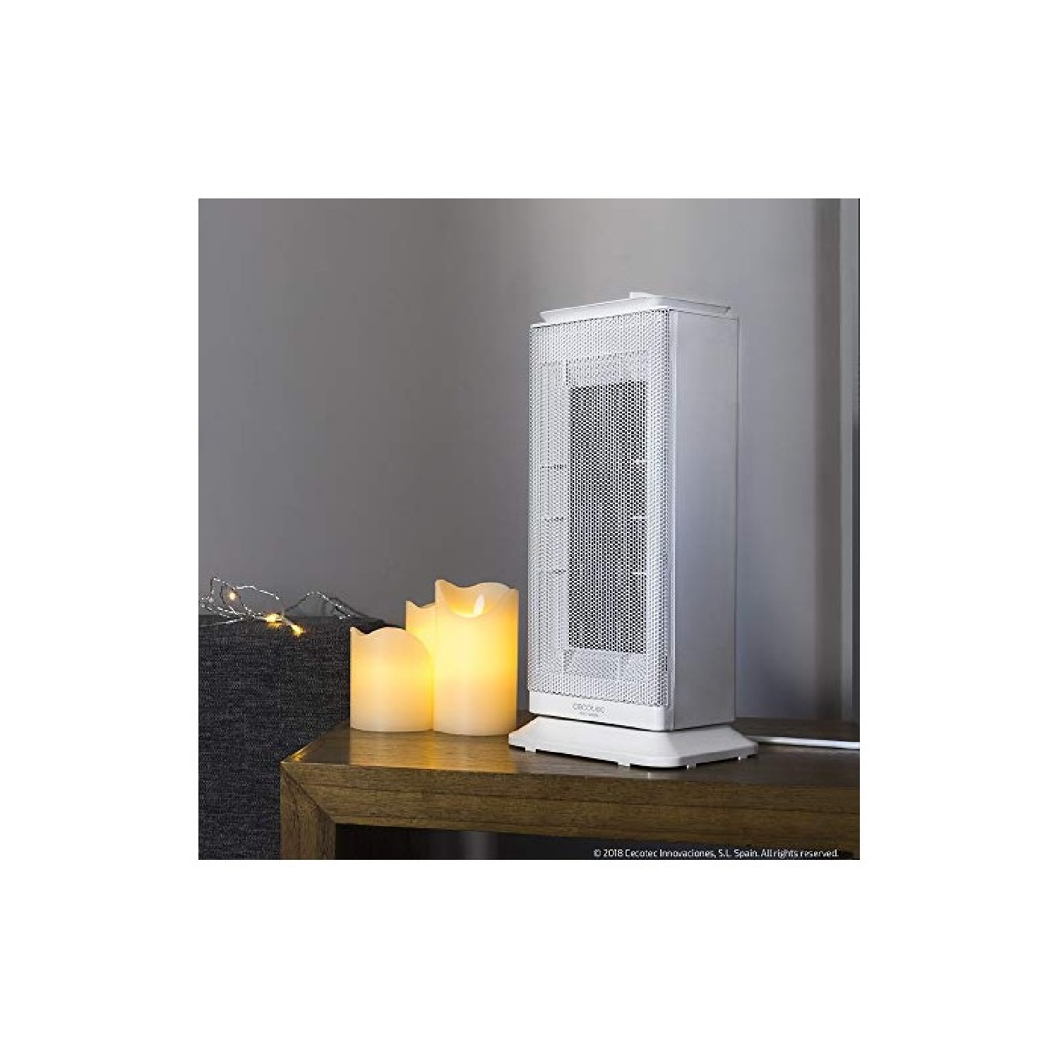 Biały grzejnik elektryczny z dwoma zapalonymi świecami na drewnianym stole. Szara ściana w tle.