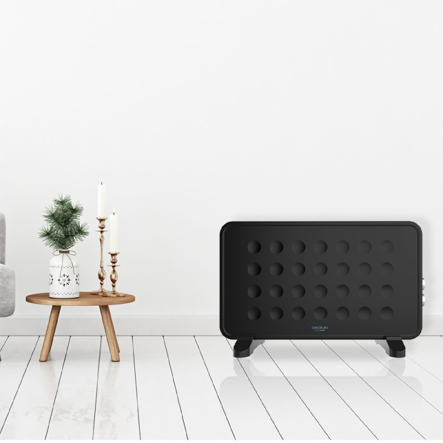 Termosifone nero con design a fori e gambe, in piedi sul pavimento. Sfondo: parete bianca e un tavolo.