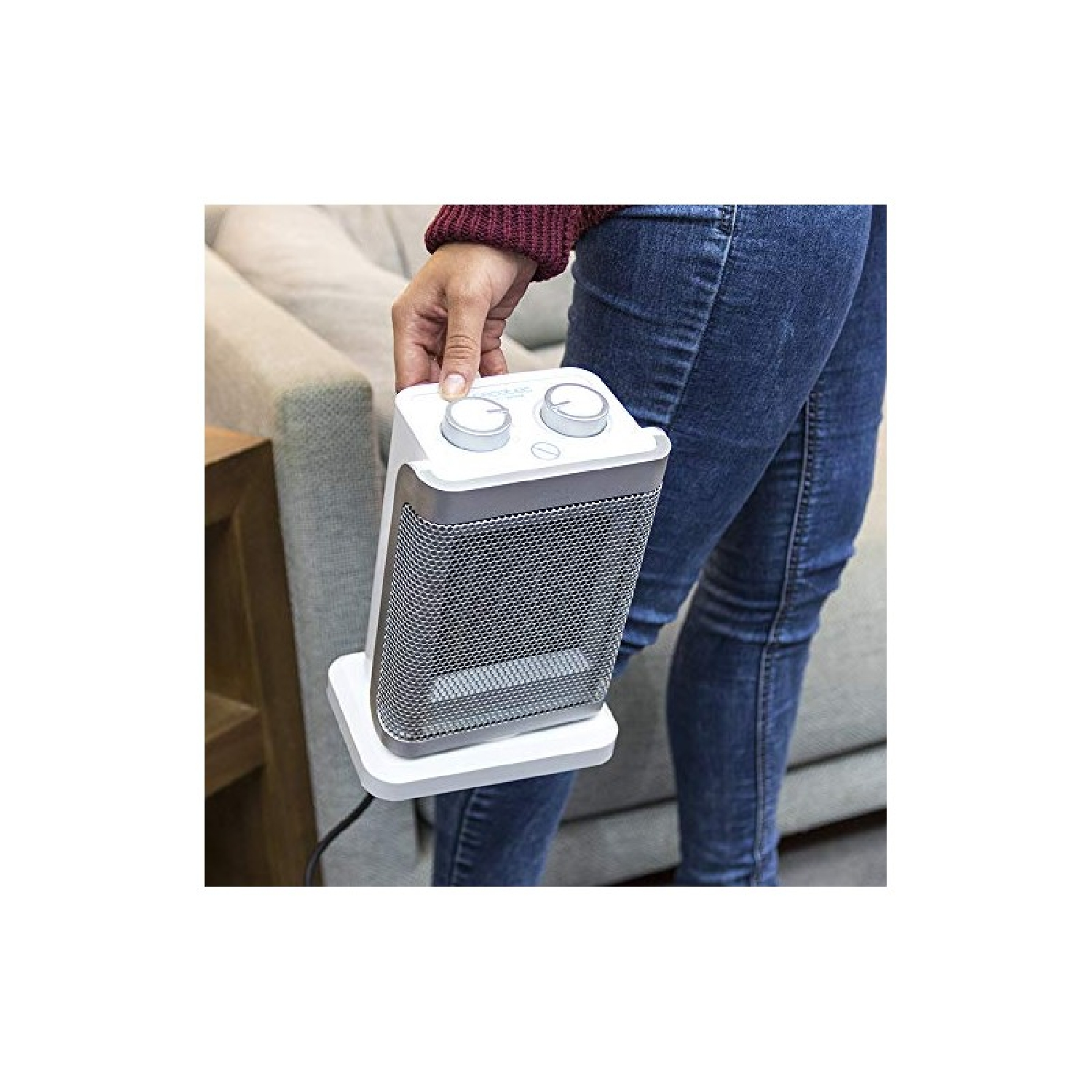 Osoba trzyma biały grzejnik z metalową siatką przed kanapą.