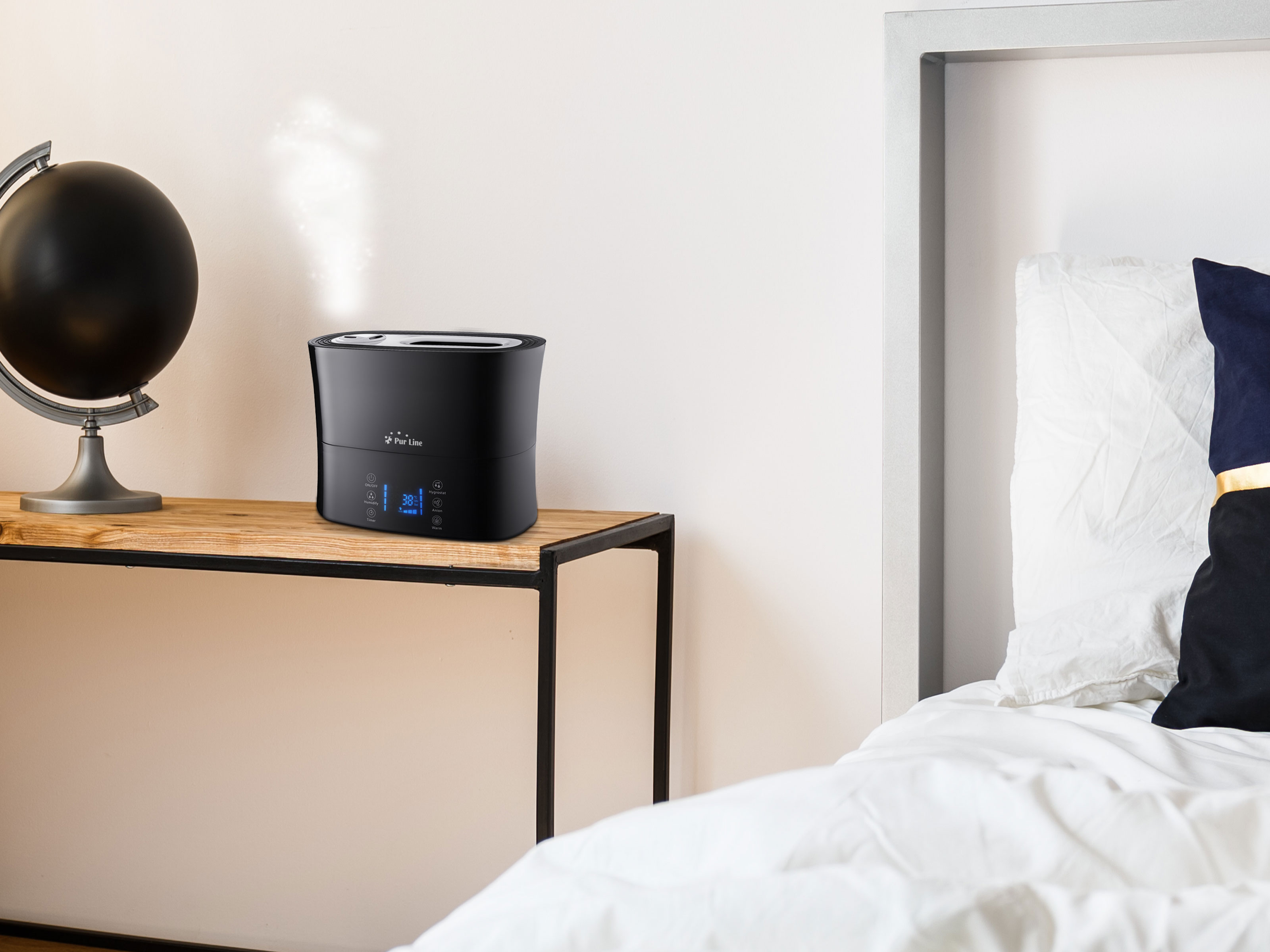 Schwarzer Luftbefeuchter auf einem Holztisch in einem Schlafzimmer. Ein Globus und ein Bett sind auch im Bild.