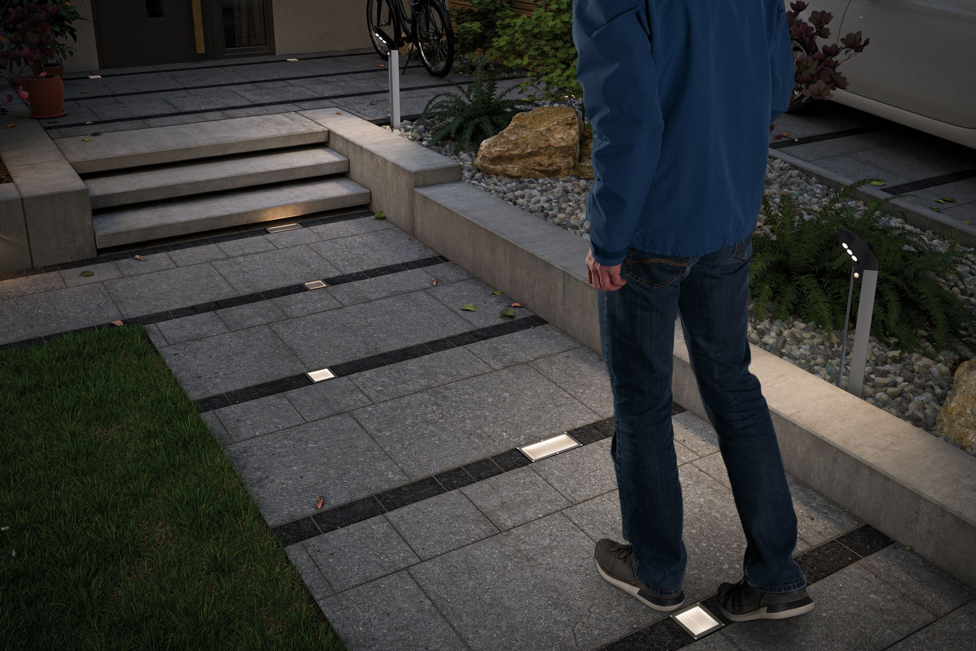 Osoba idąca kamiennym chodnikiem ze światłami. Rower zaparkowany w tle.