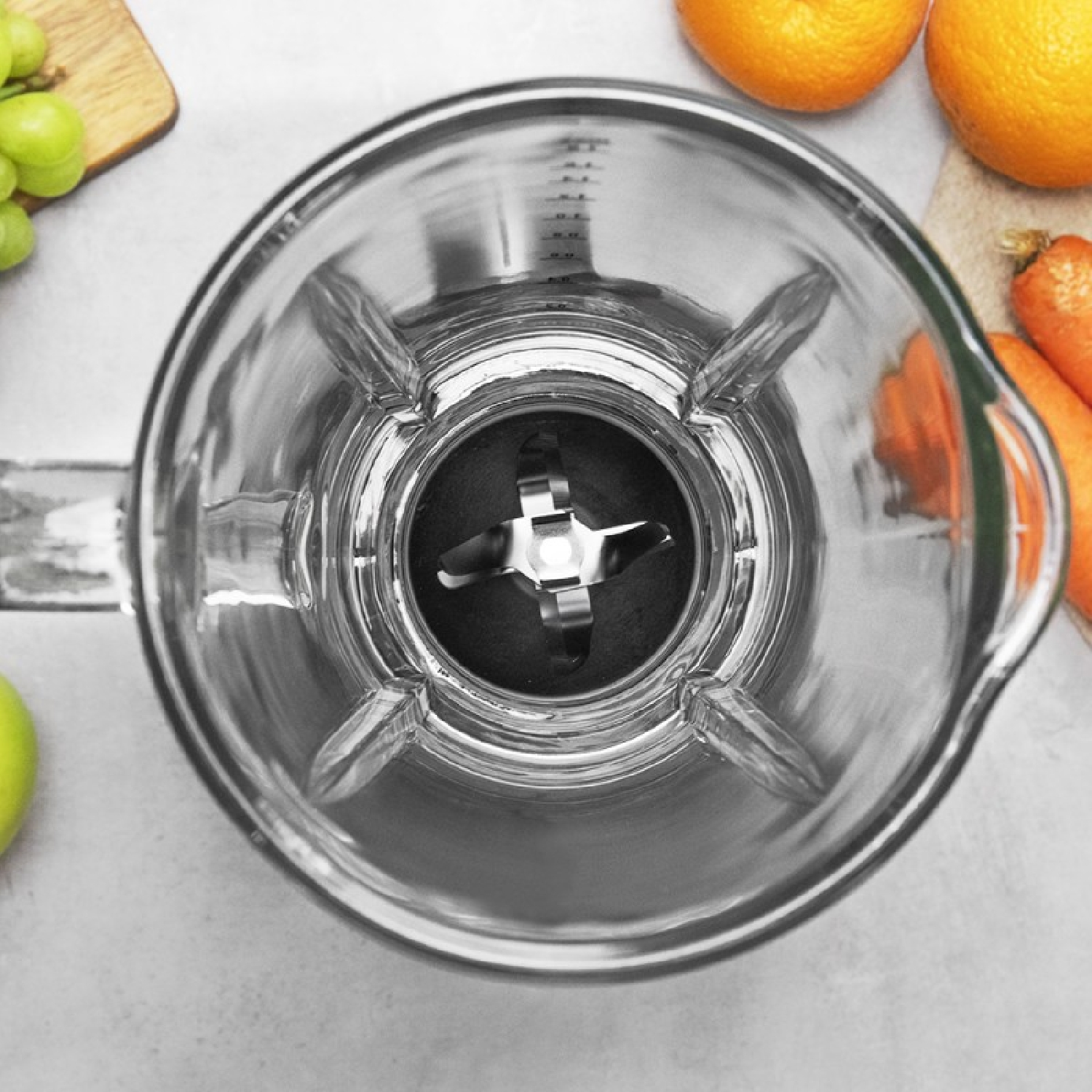 Blender z ostrzami widziany z góry. Owoce takie jak pomarańcze i jabłka otaczają go.