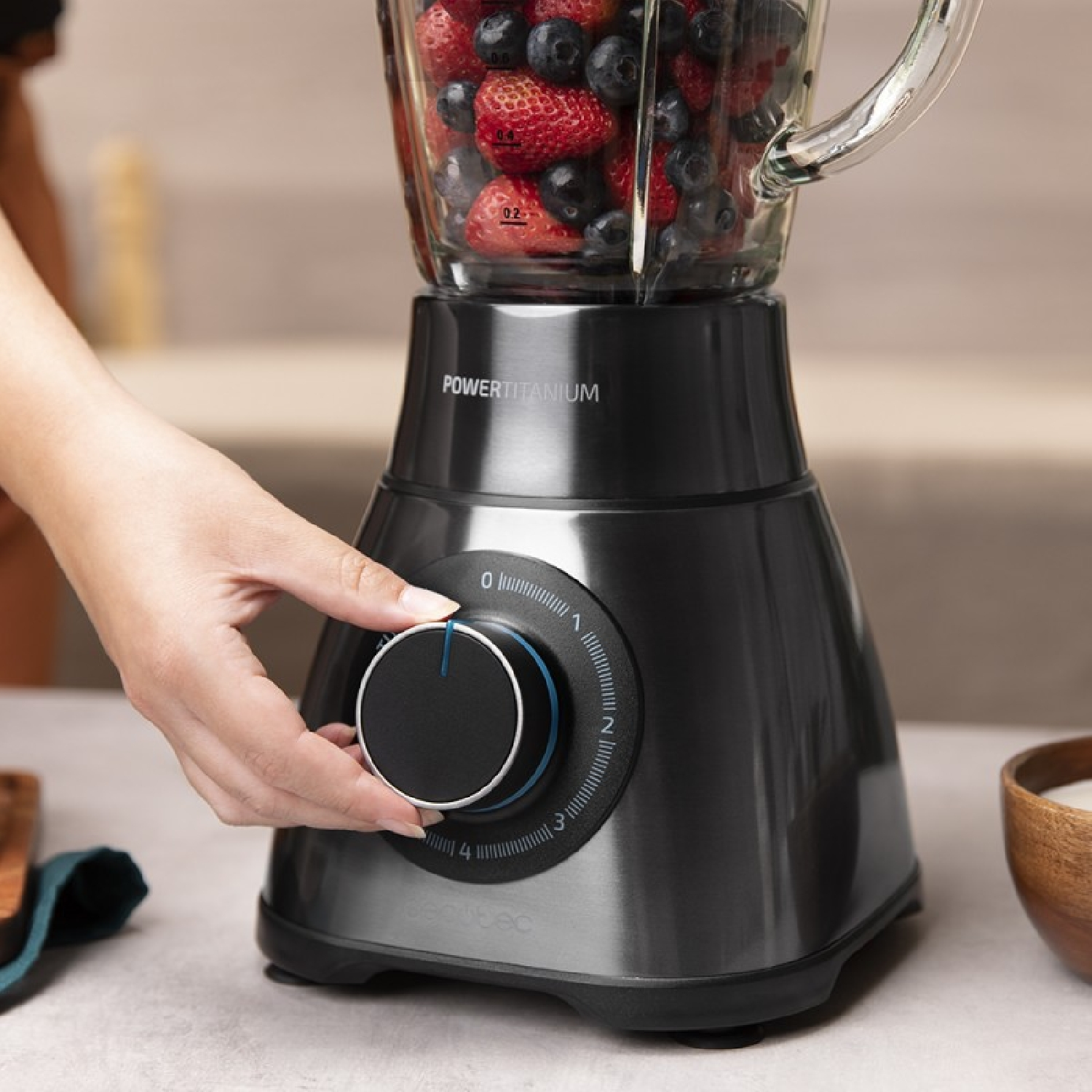 Ręka osoby reguluje pokrętło prędkości czarnego blendera wypełnionego jagodami.
