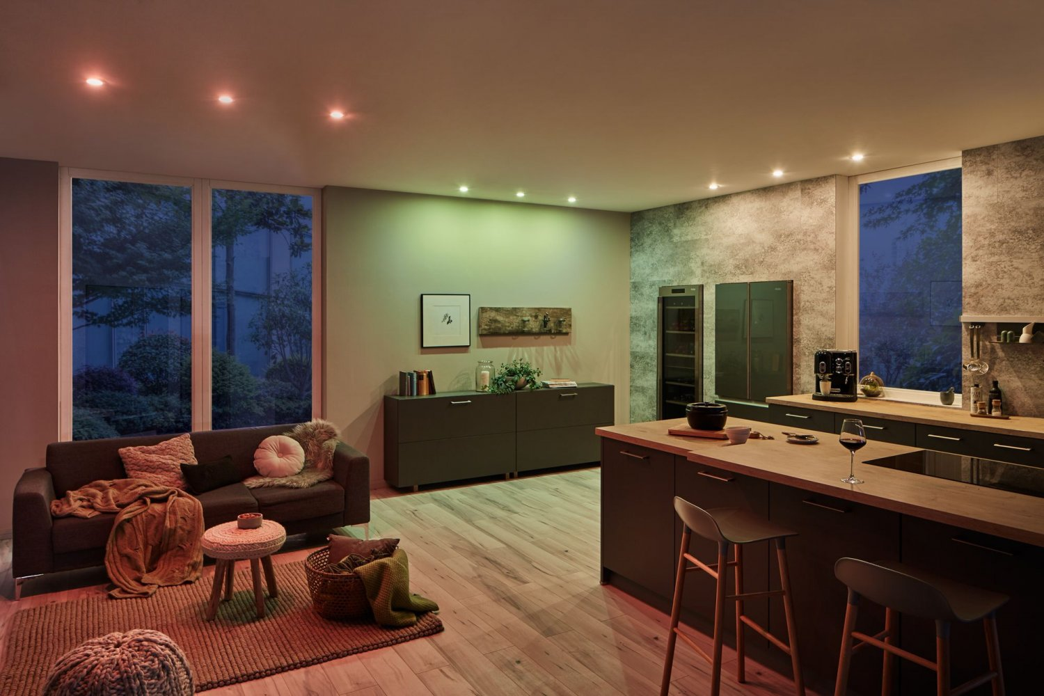 Eine moderne Küche mit Sofa, Insel und Einbauleuchten. Die Fenster zeigen eine Nachtansicht.