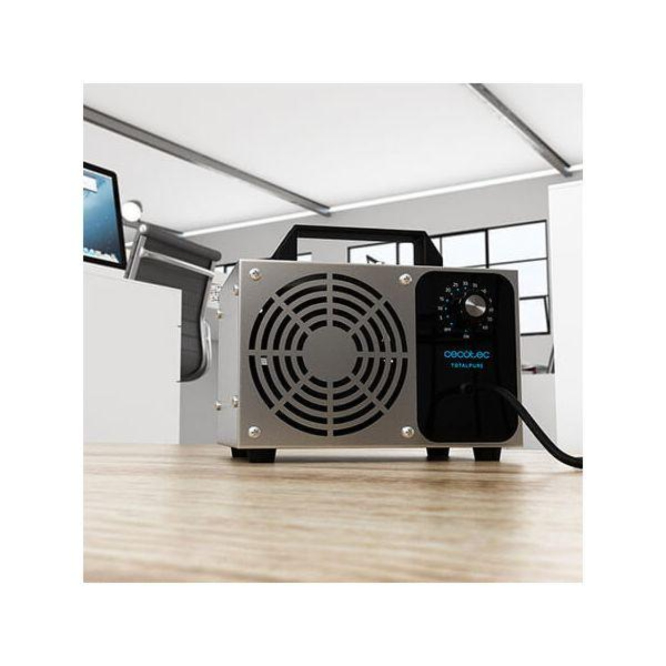 Purificador de aire plateado con asa, ventilador y panel de control. Está sobre un escritorio de madera.