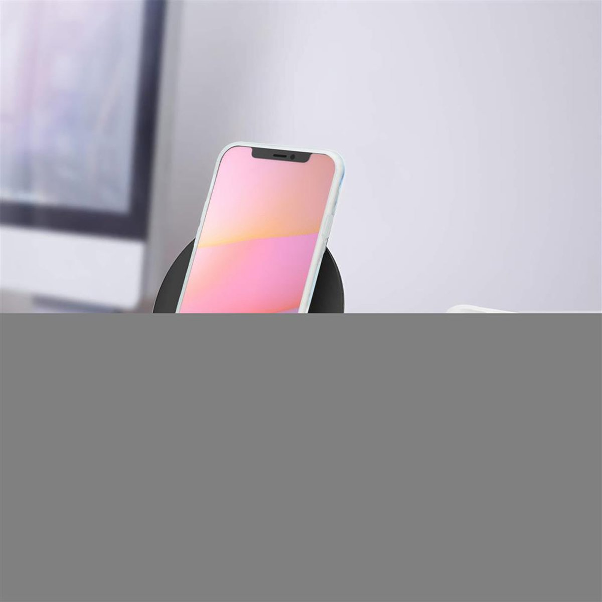 Un telefono è su un caricatore wireless. Lo sfondo è grigio chiaro. Il telefono ha uno schermo rosa.