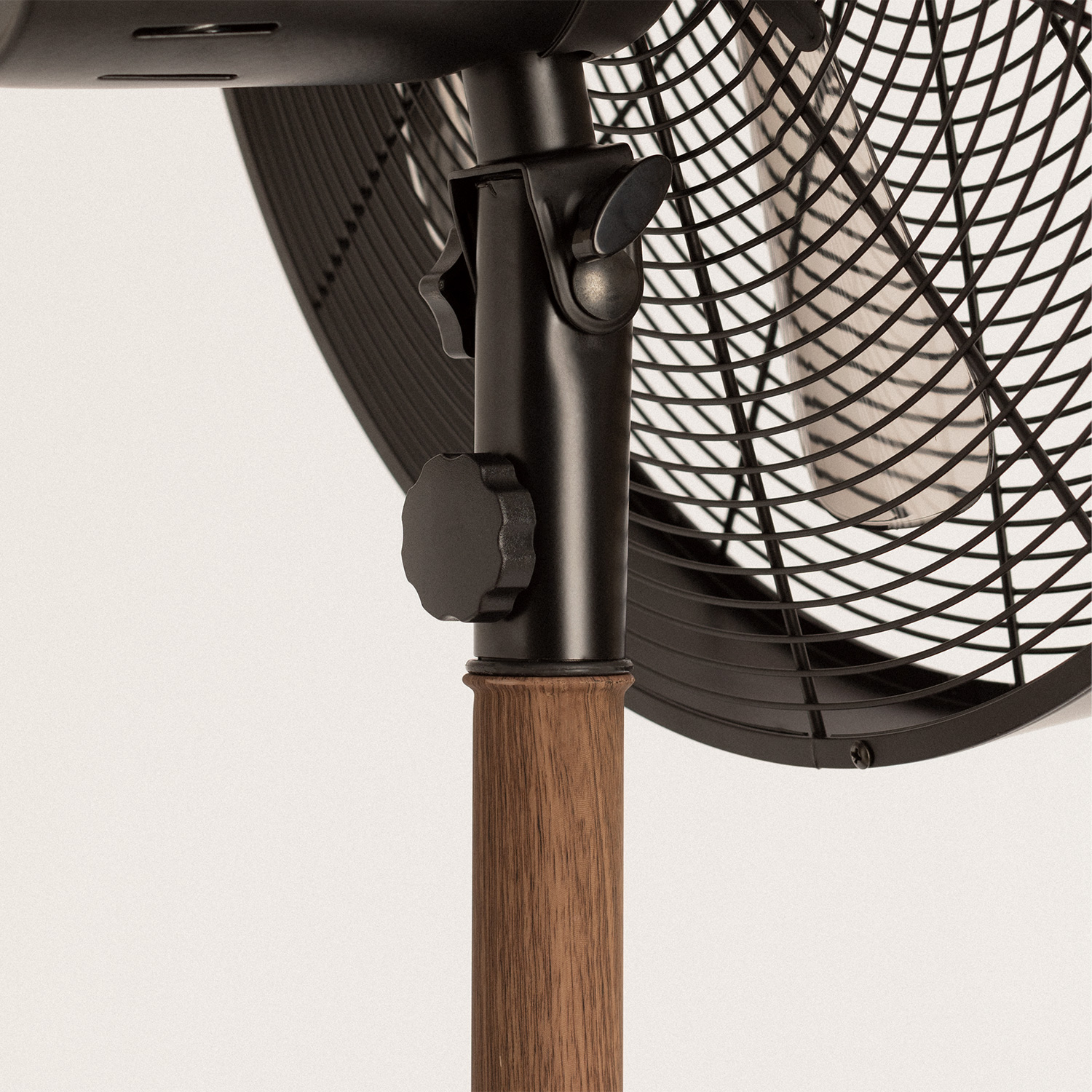 Primer plano de la base de un soporte de ventilador negro y marrón. Base de grano de madera y poste negro.