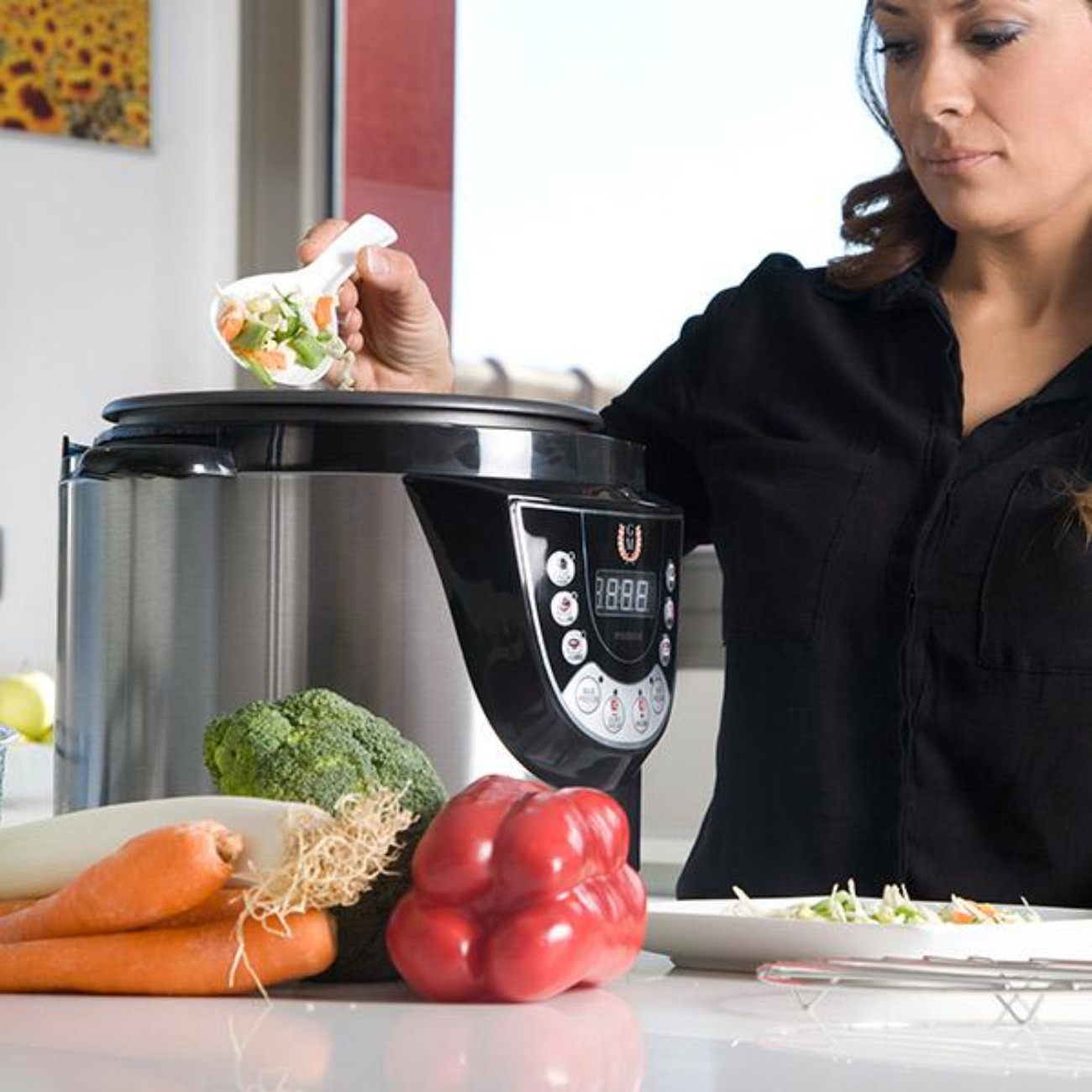 Donna aggiunge verdure a una pentola a pressione. Verdure come carote, broccoli e peperoni rossi sono sul bancone.