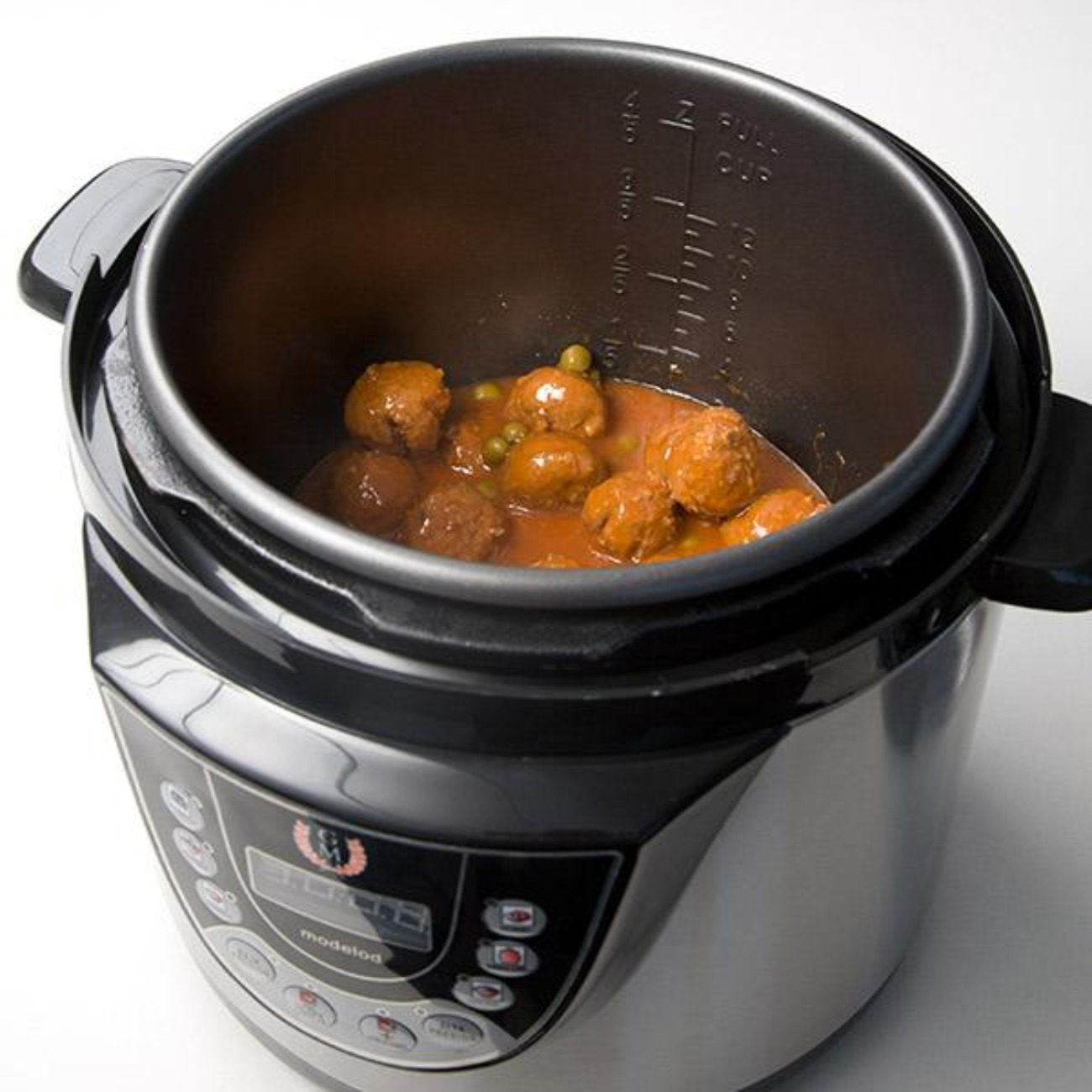 Una pentola a pressione piena di polpette e piselli in salsa rossa.