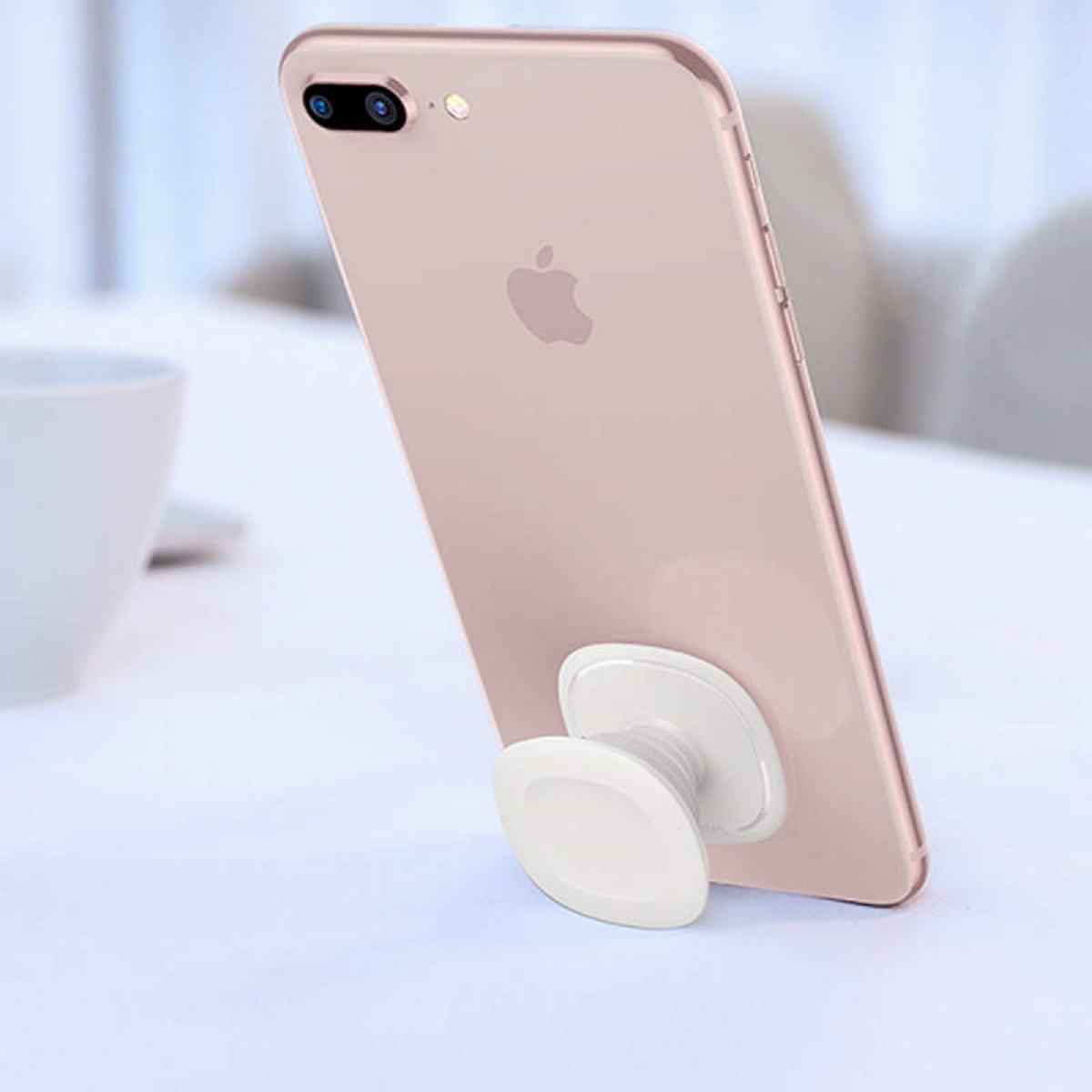 Rosa iPhone mit weißem Pop-Socket. Das Telefon liegt auf einer weißen Oberfläche. Das Apple-Logo ist sichtbar.