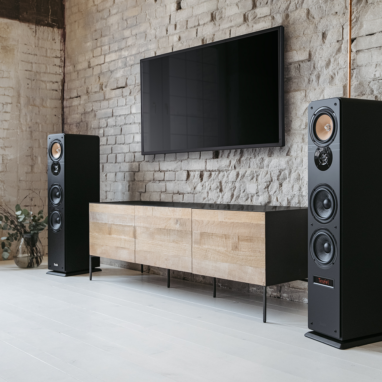 Ein Wohnzimmer mit einem Fernseher an der Wand, einem Holzschrank und zwei hohen schwarzen Lautsprechern.