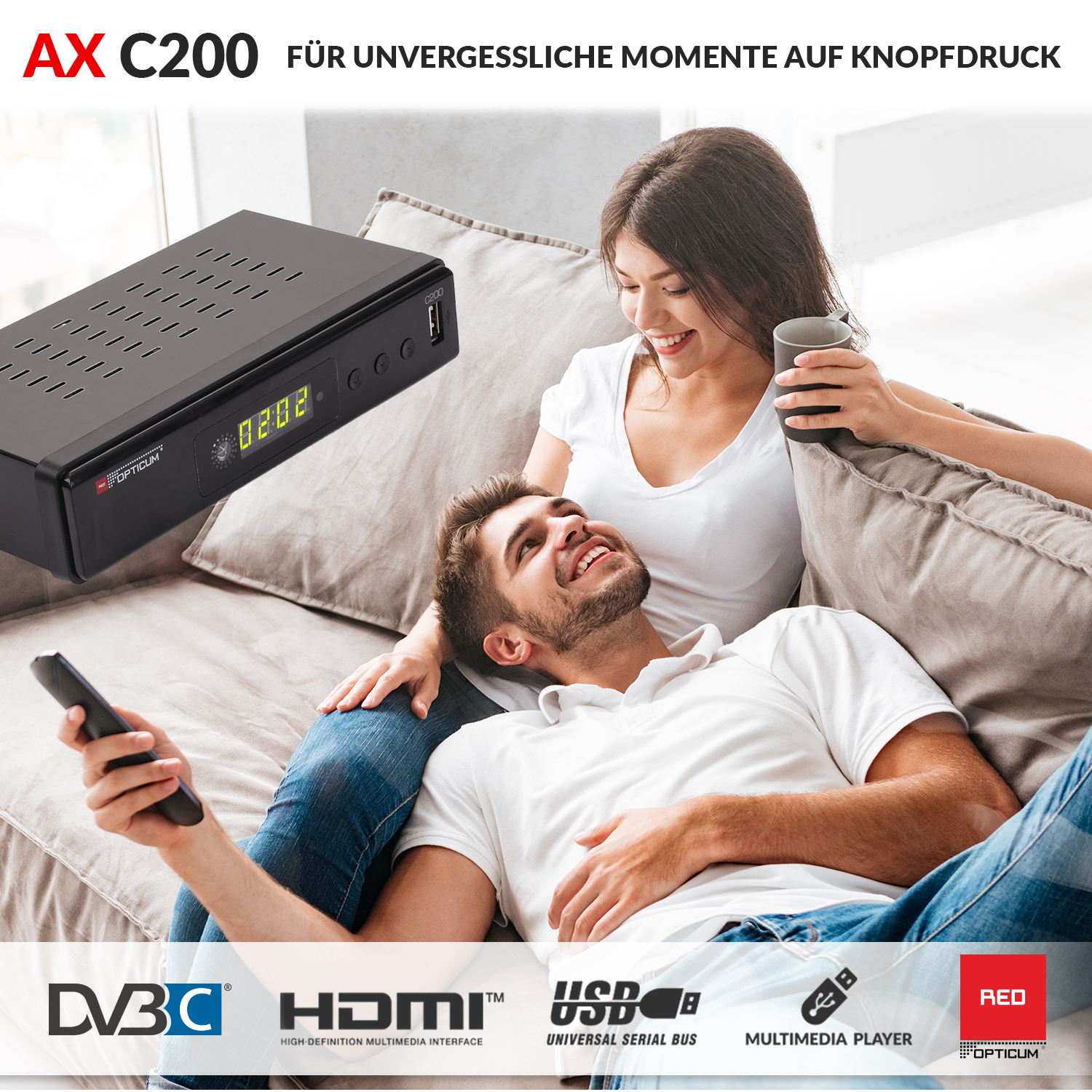 Ein Paar sitzt auf einem Sofa. Ein schwarzes Gerät steht auf dem Couchtisch vor ihnen. Logos sind sichtbar.