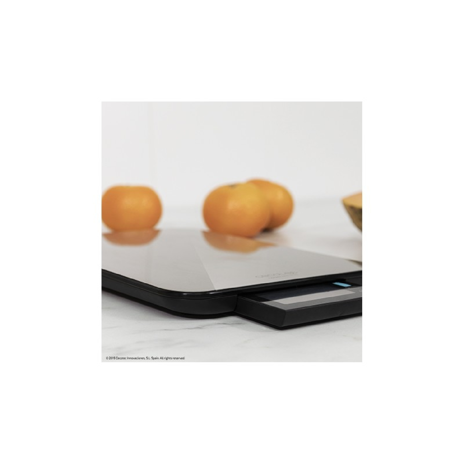 Czarna waga cyfrowa z pomarańczami. Waga stoi na marmurowej powierzchni.