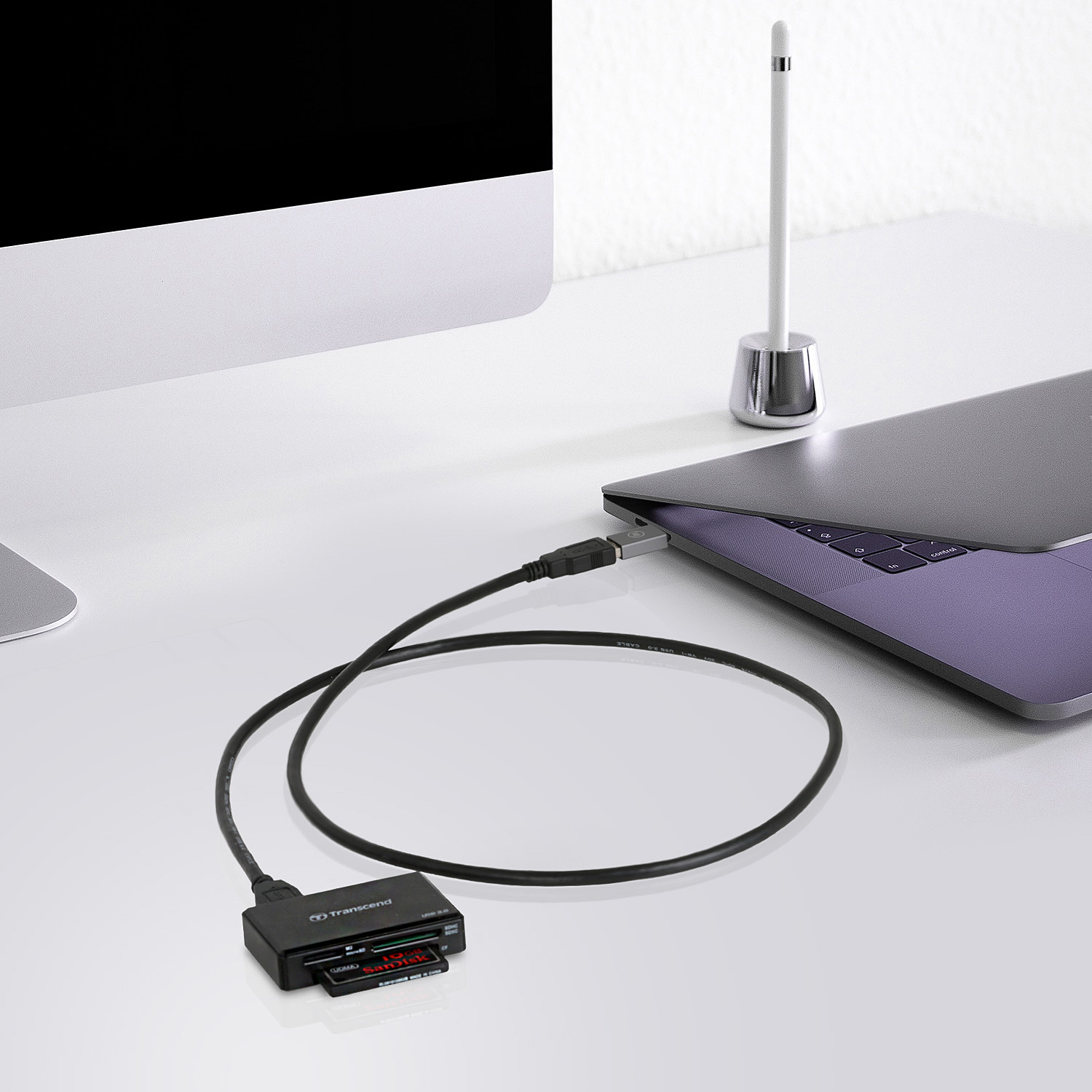 Ein schwarzer Kartenleser, der über ein Kabel mit einem Laptop verbunden ist. Ein weißer Schreibtisch.