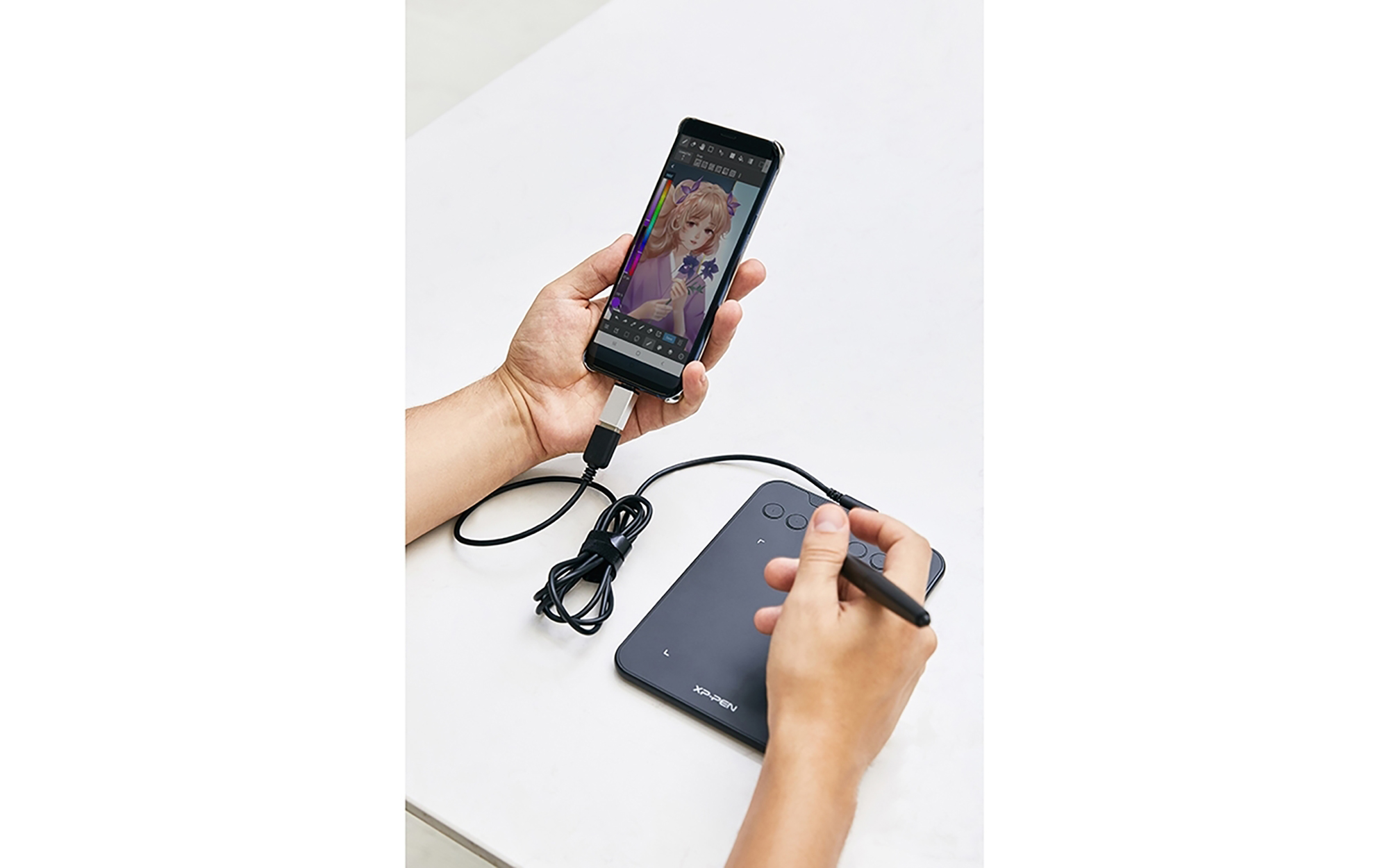 Osoba trzymająca telefon i podłączony tablet z rysikiem. Telefon pokazuje aplikację do tworzenia sztuki.