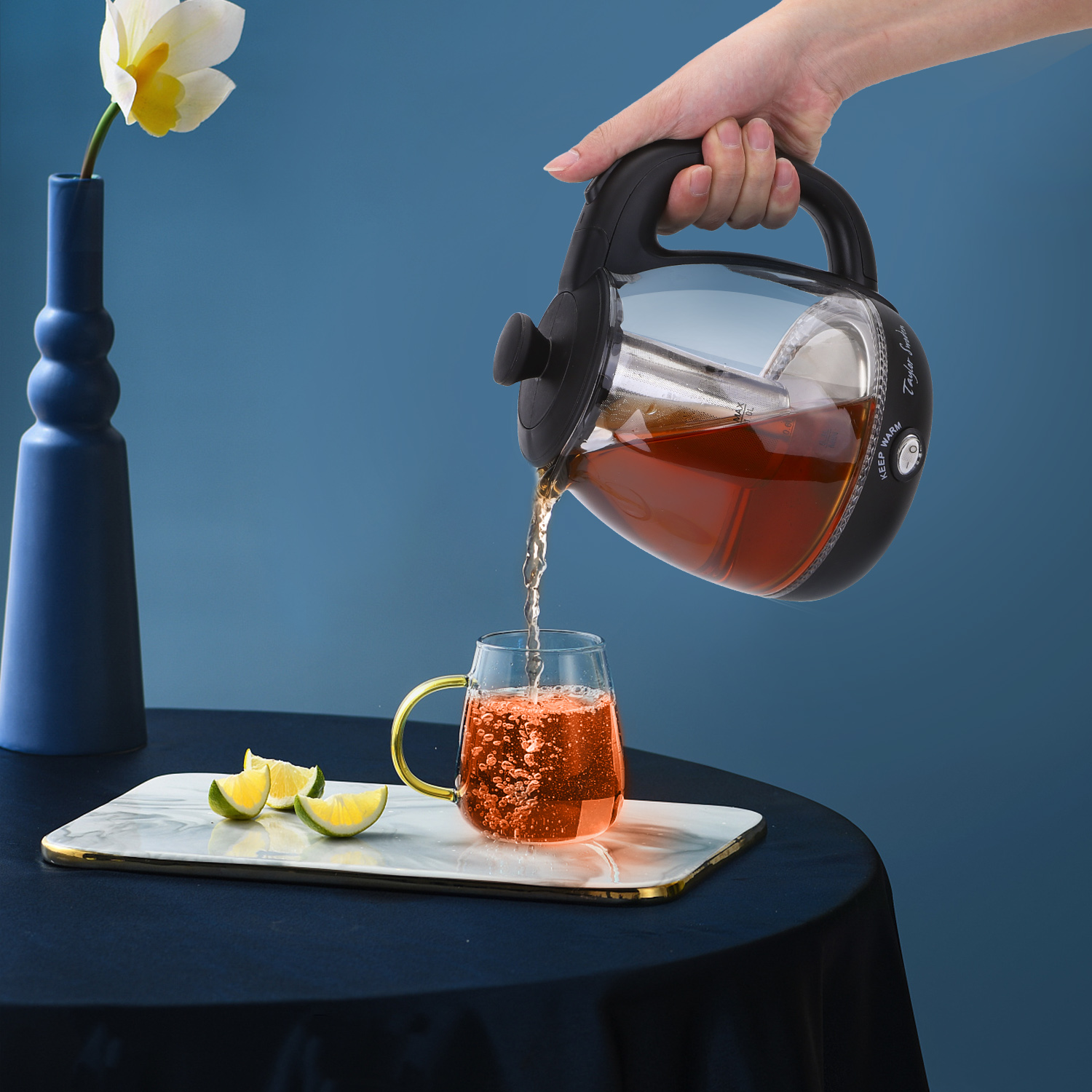 Eine Hand gießt Tee aus einem Wasserkocher in ein Glas, mit einem Tablett mit Zitronen.