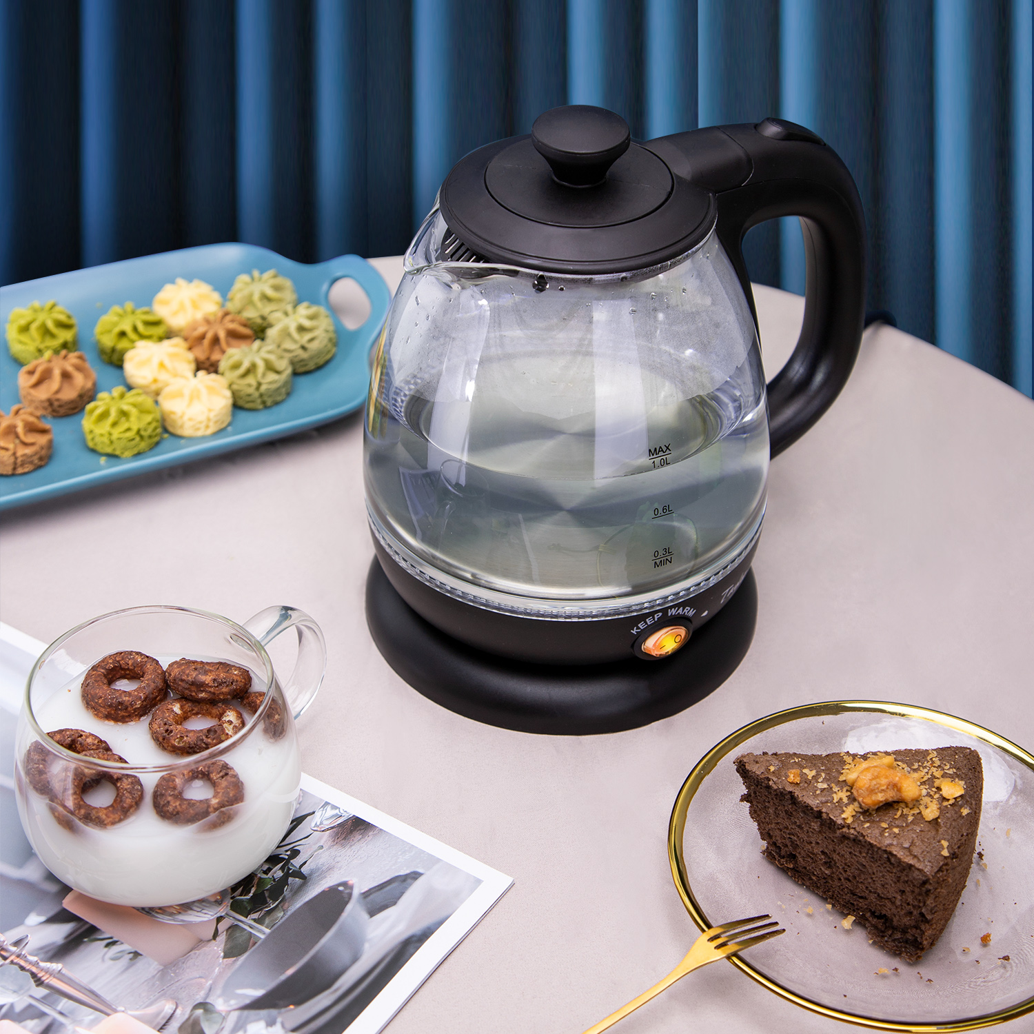 Elektrischer Wasserkocher mit Wasser, Keksteller, Müsli mit Milch im Glas und ein Stück Kuchen.