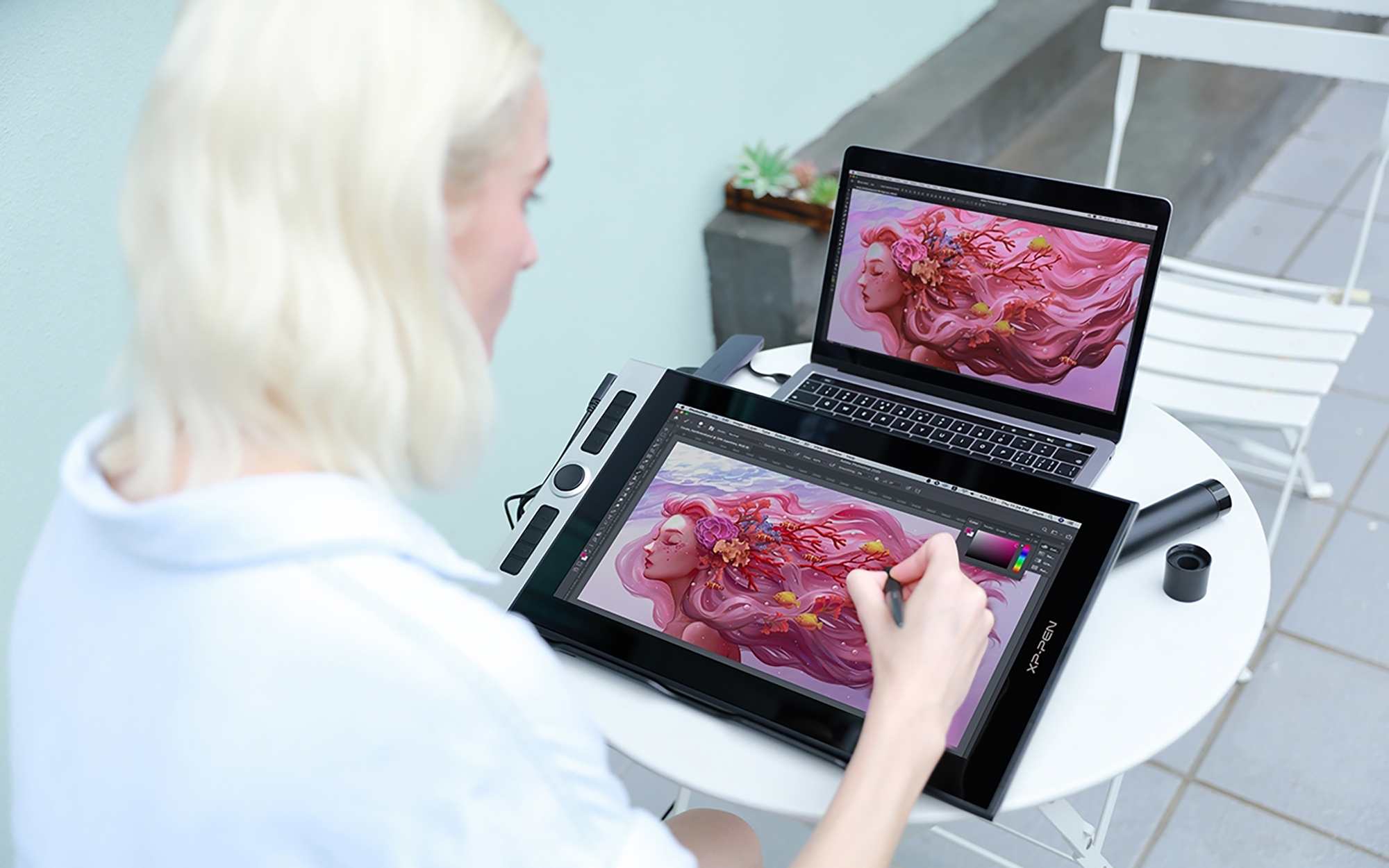 Una mujer usando una tableta de arte digital y un portátil, con una pintura digital colorida.