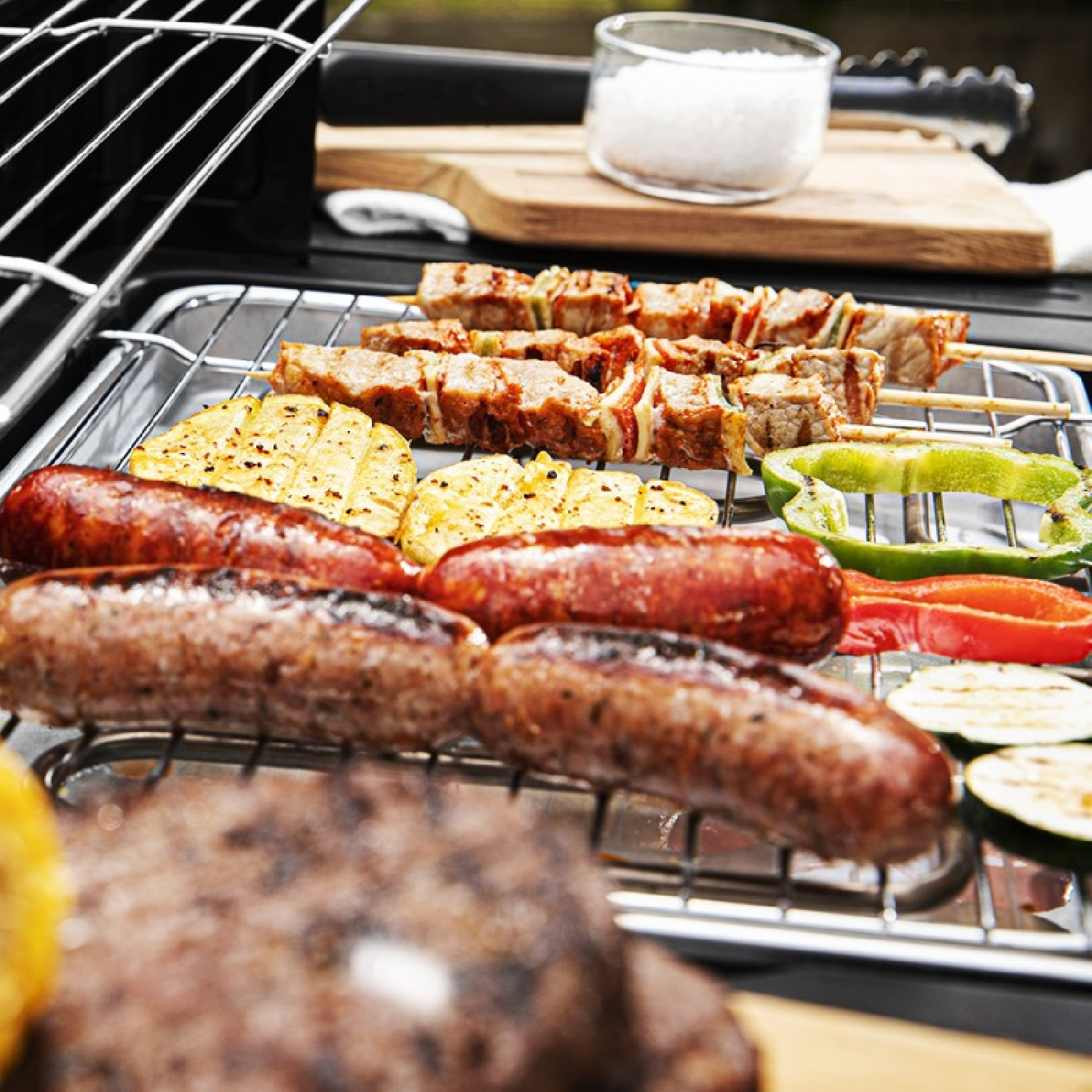 Gegrillte Würstchen, Kartoffeln und Gemüse auf einem Grill.