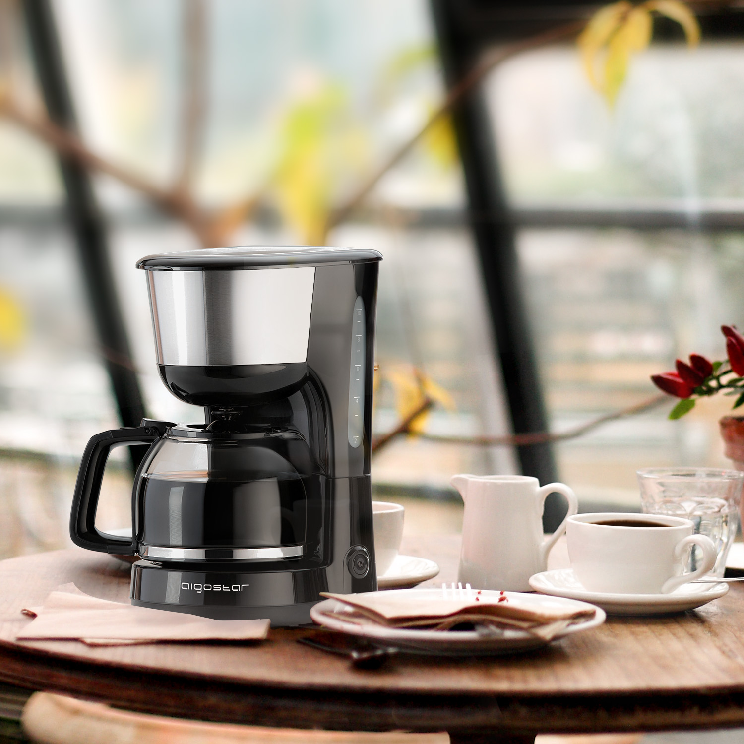 Kaffeemaschine auf einem Tisch mit Tassen, Sahne und einem Fenster im Hintergrund.