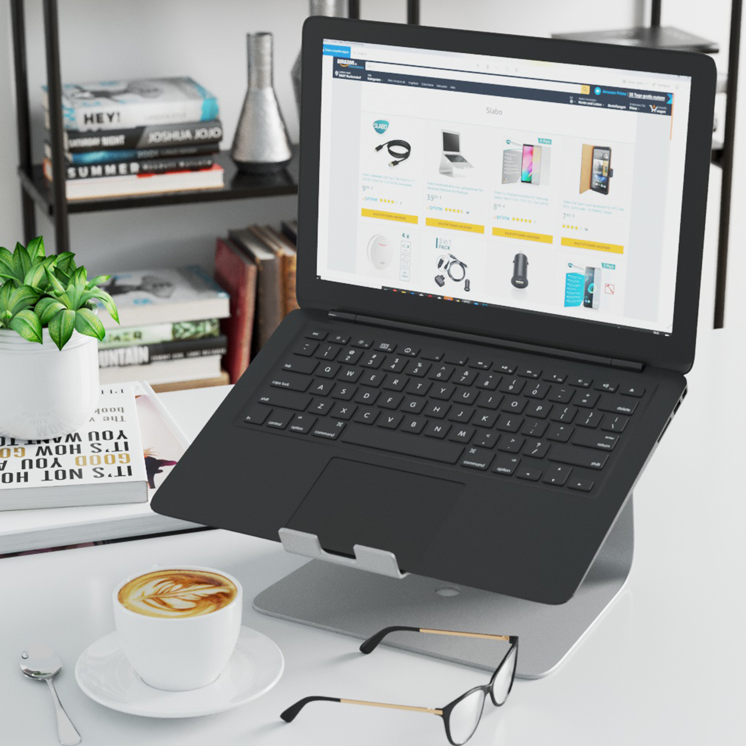 Laptop auf einem Ständer mit Kaffeetasse, Brille und Büchern. Eine Website ist auf dem Bildschirm geöffnet.