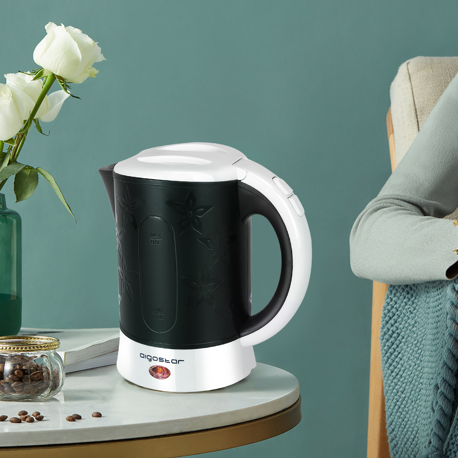 Hervidor eléctrico blanco y negro con diseño floral en mesa con granos de café.