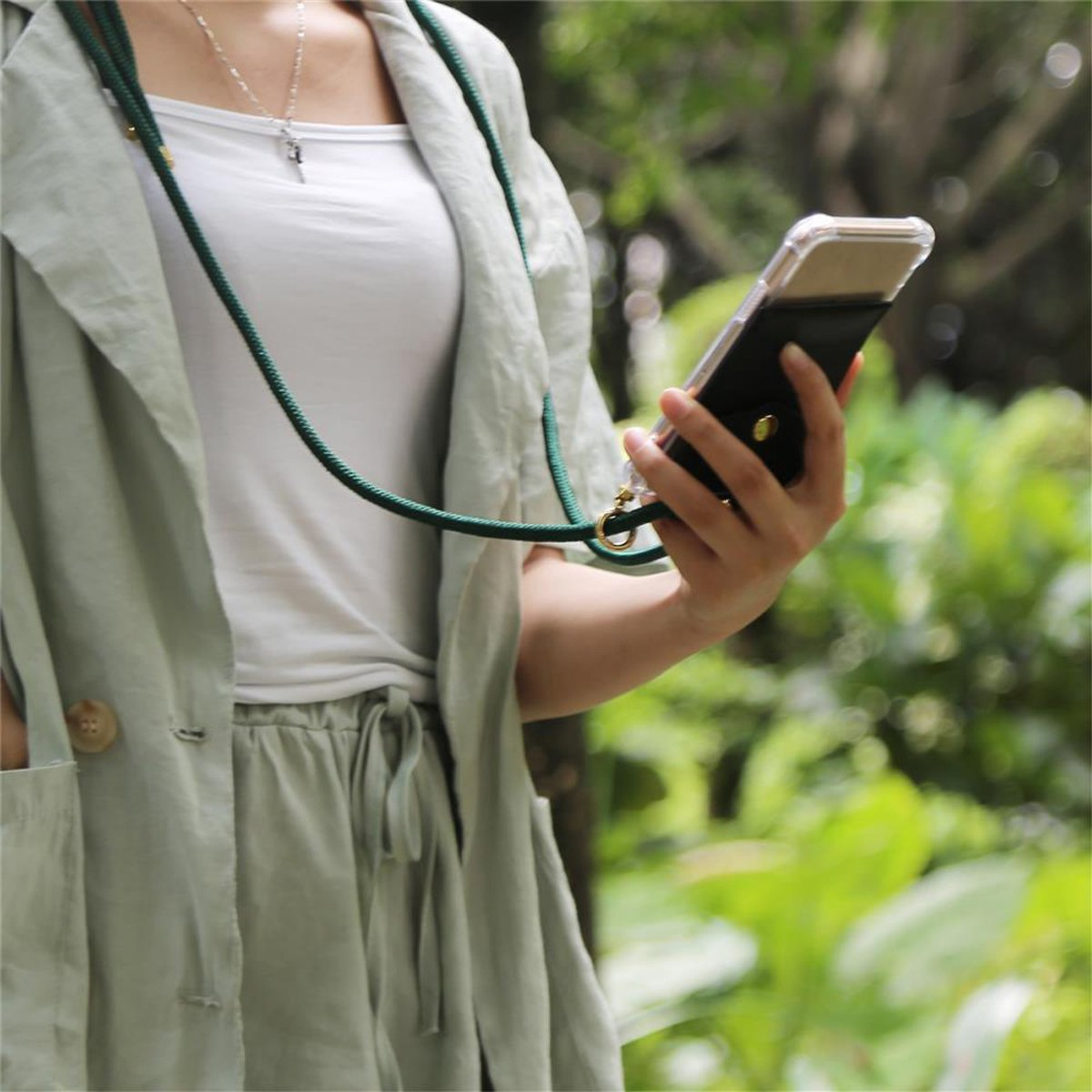 Una persona tiene in mano un telefono con custodia e cordino. Lo sfondo è verde sfocato.