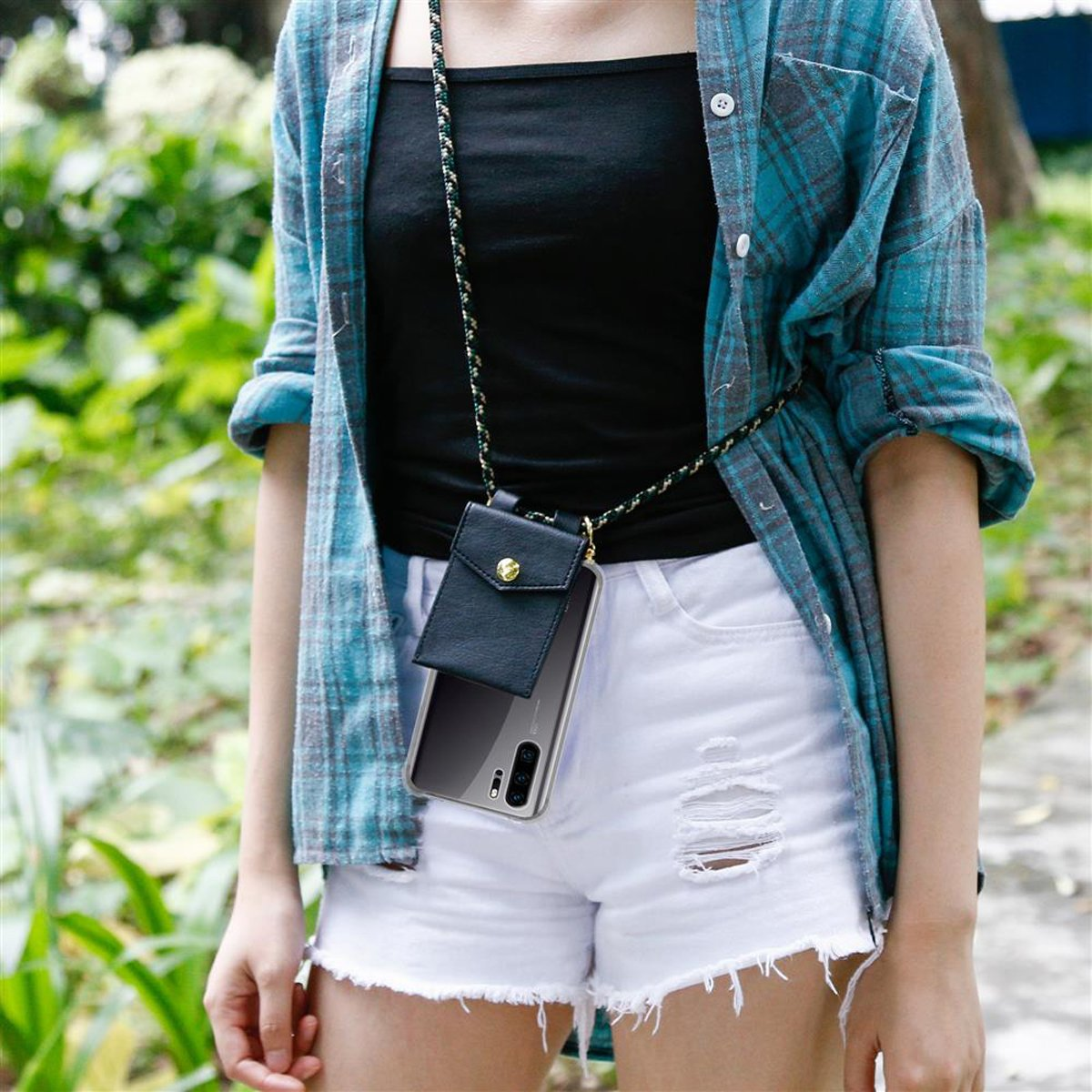 Persona con camicia a quadri verde acqua, top nero e pantaloncini bianchi, che porta una custodia per telefono con cinturino nero.