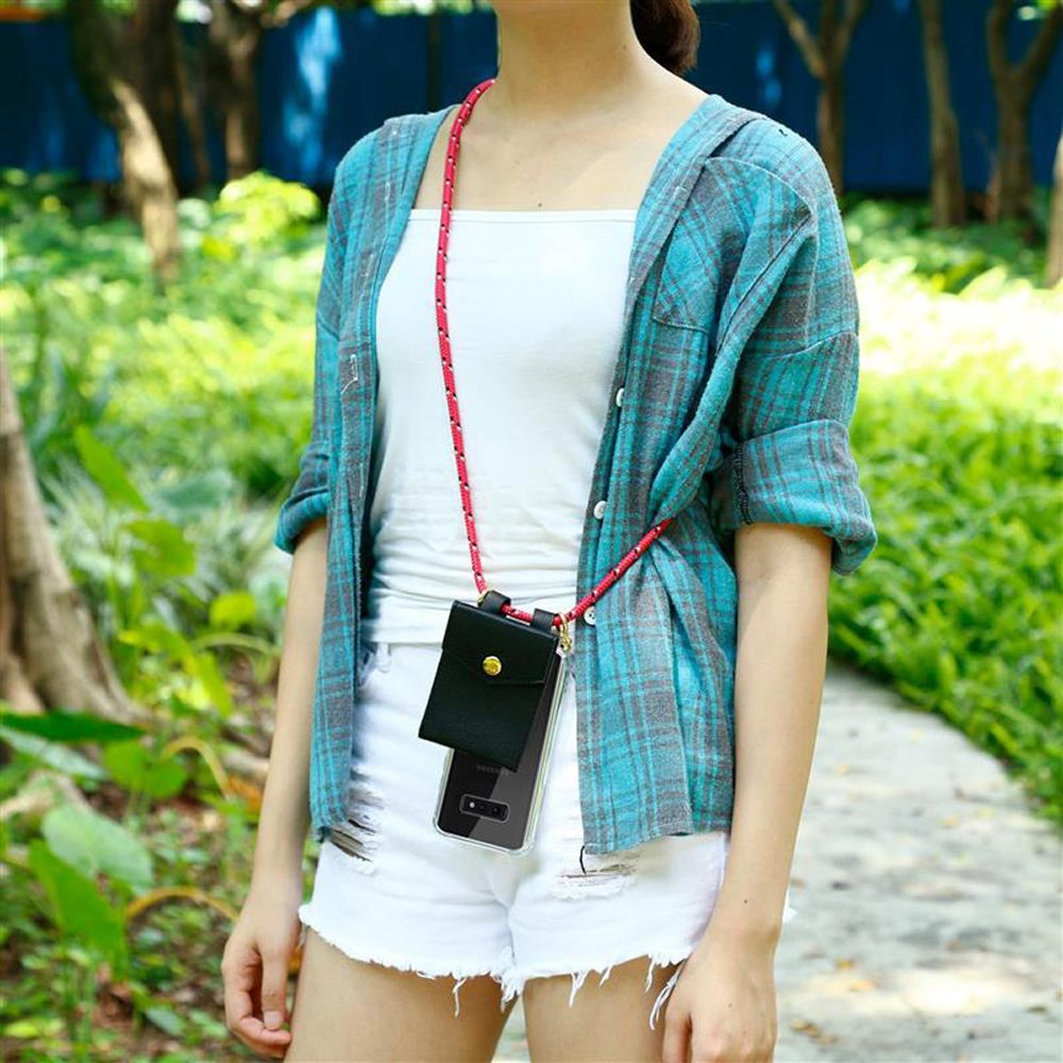 Donna in pantaloncini con telefono su cinturino rosso. Camicia turchese su top bianco. Fogliame verde sullo sfondo.
