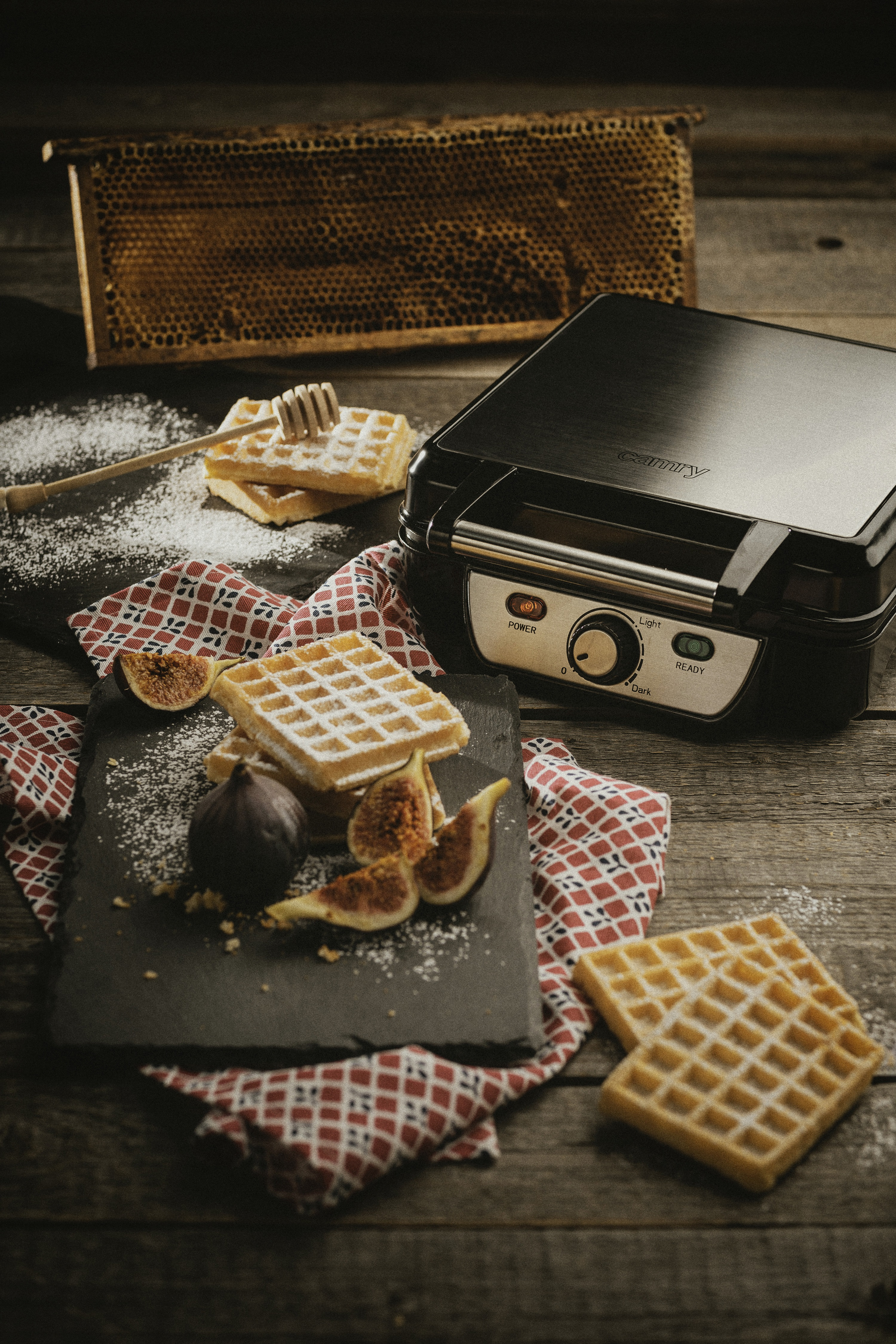 Drewniany stół z goframi, figami i gofrownicą. Obecny jest również plaster miodu i nabierak do miodu.