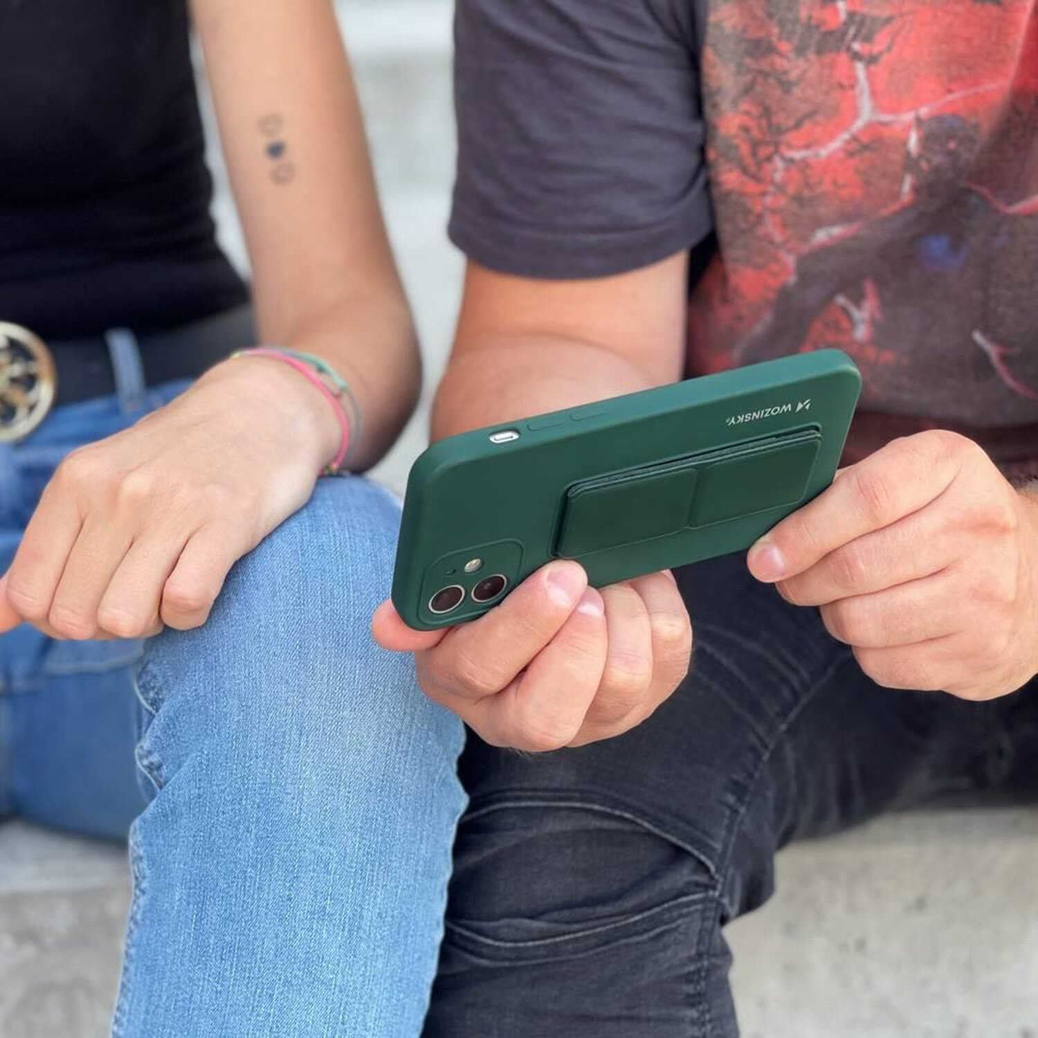 Eine Person hält ein grünes Telefon mit einem Pop-out-Griff. Eine andere Person ist teilweise sichtbar.