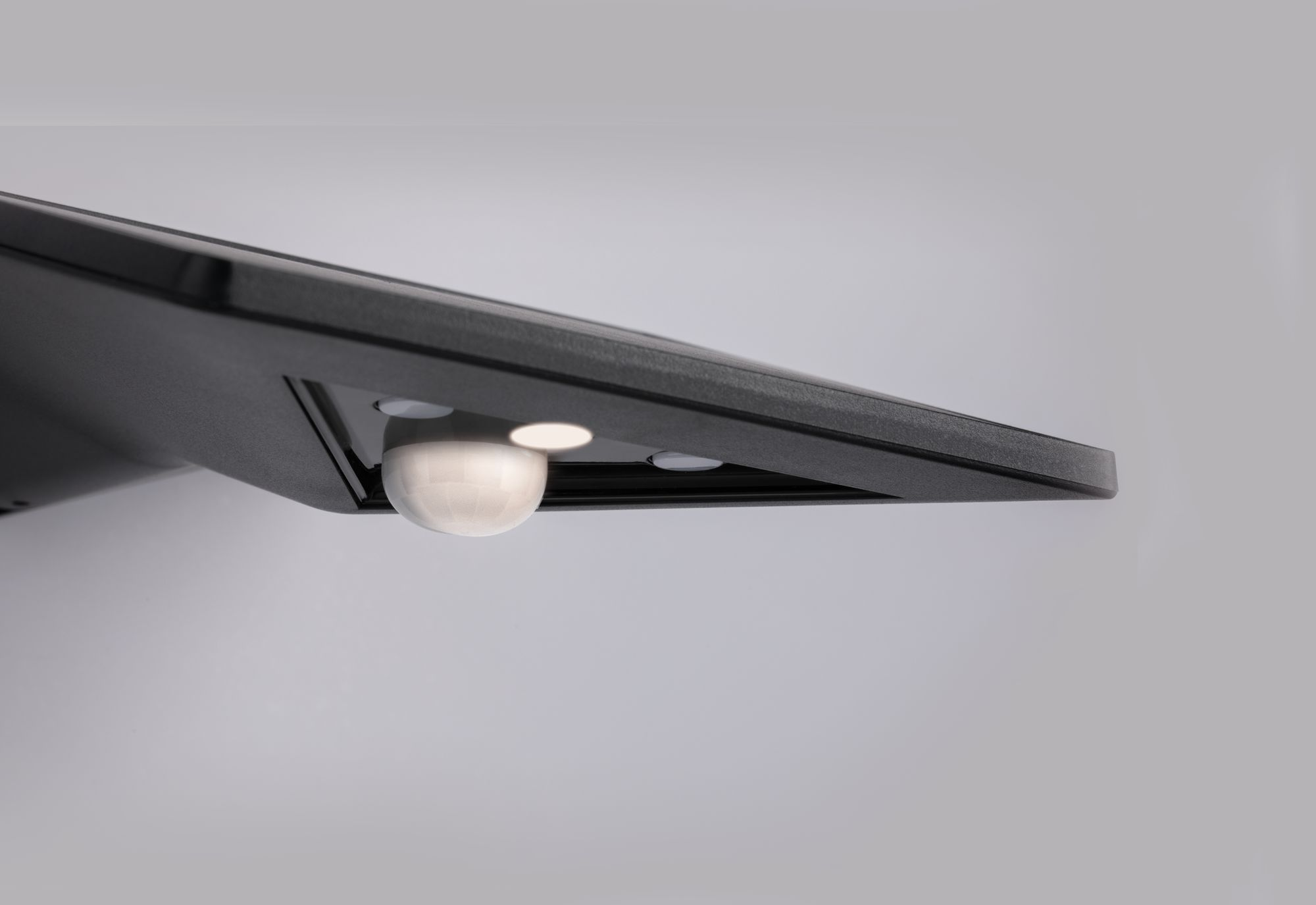 Zbliżenie czarnego czujnika ze światłem, prawdopodobnie czujnik ruchu na białej ścianie.