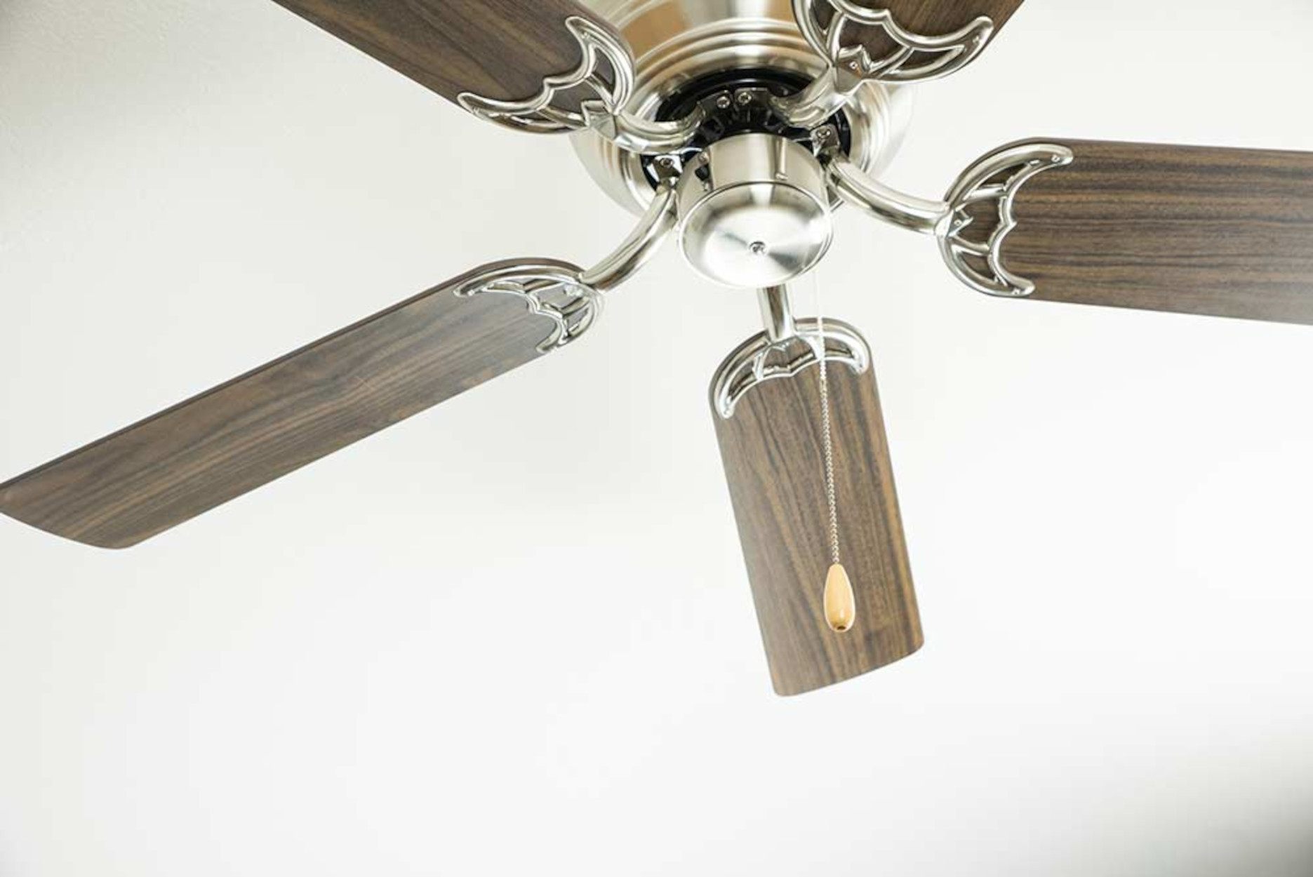 Un ventilatore da soffitto con pale in legno e un centro in metallo, appeso a un soffitto bianco.