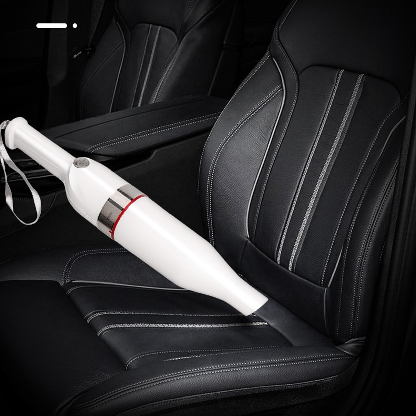 Weißer Handstaubsauger auf einem schwarzen Autositz. Roter Akzent am Gehäuse.