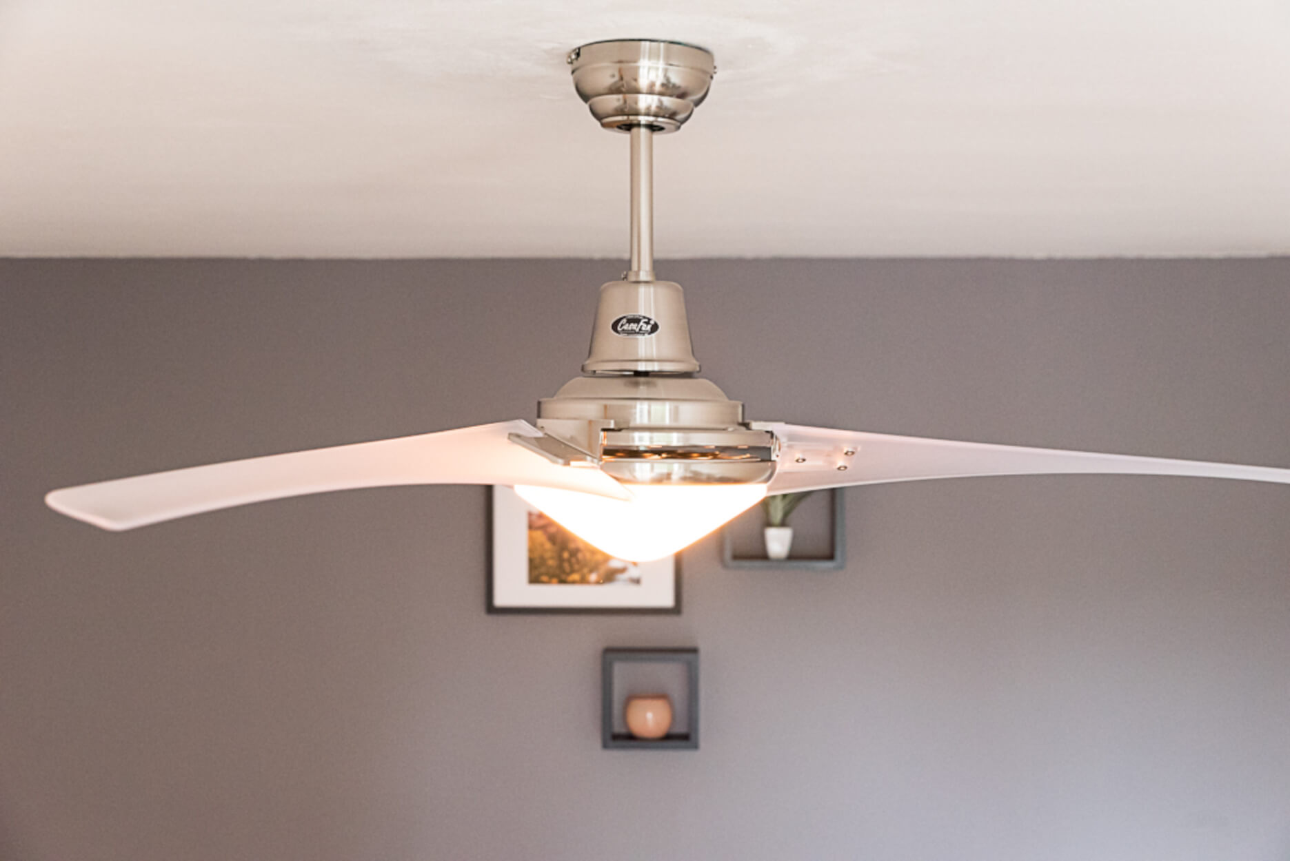 Deckenventilator mit Leuchte, an einer weißen Decke montiert. Der Raum hat graue Wände und Dekoration.