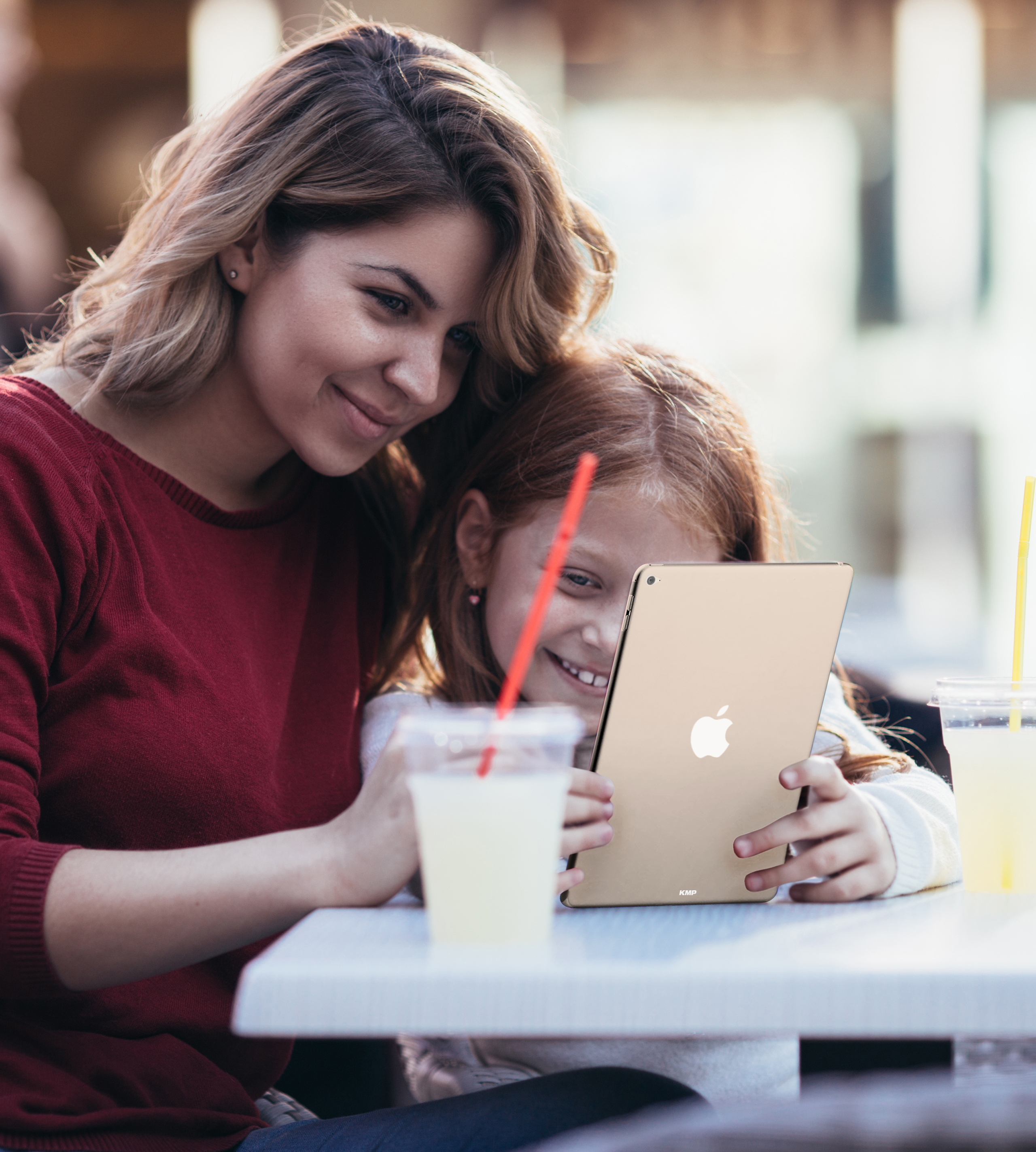 Mutter und Tochter schauen auf ein goldenes Tablet mit Apple-Logo an einem Tisch im Freien.