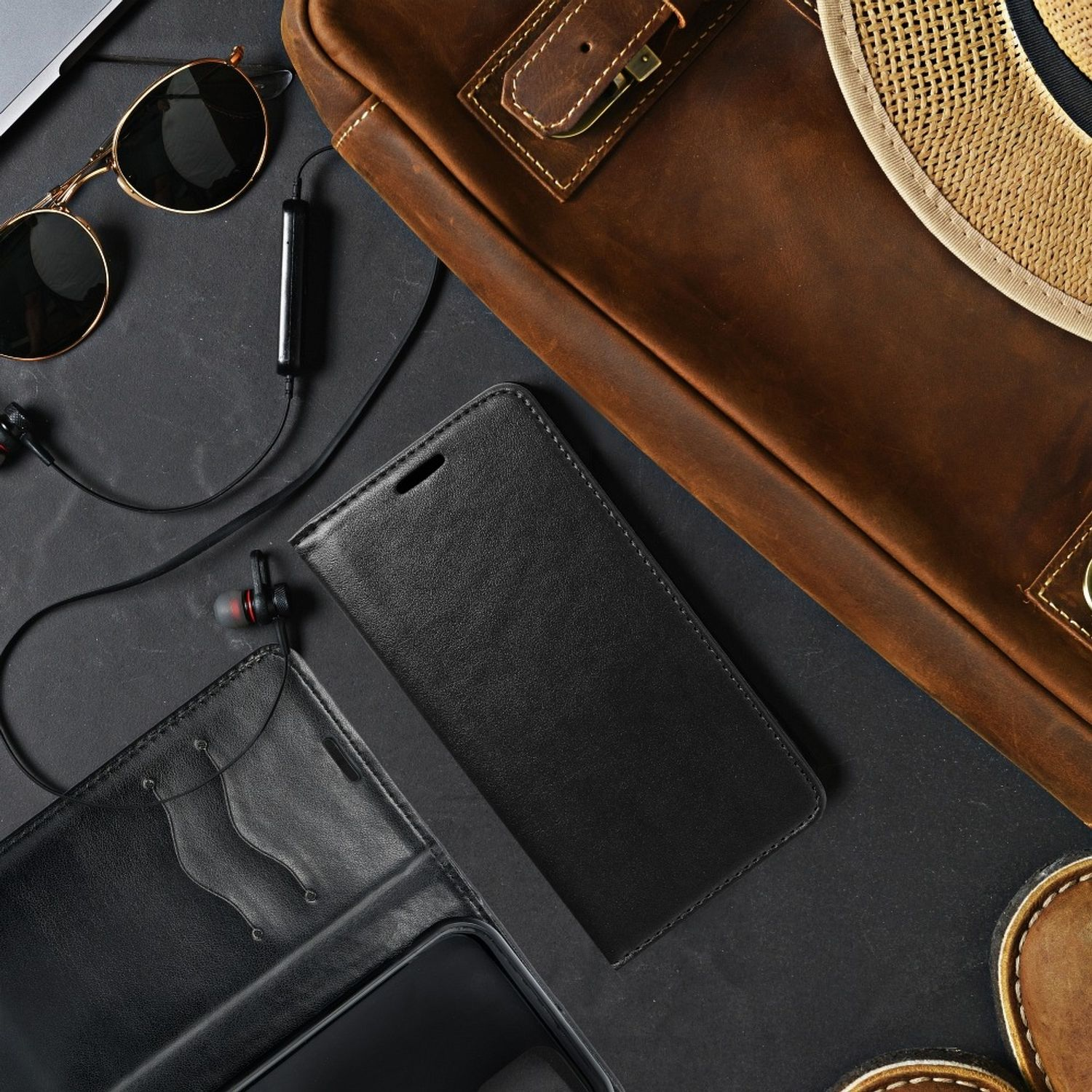 Schwarze Leder-Handyhülle mit Zubehör, darunter Sonnenbrille und Kopfhörer.