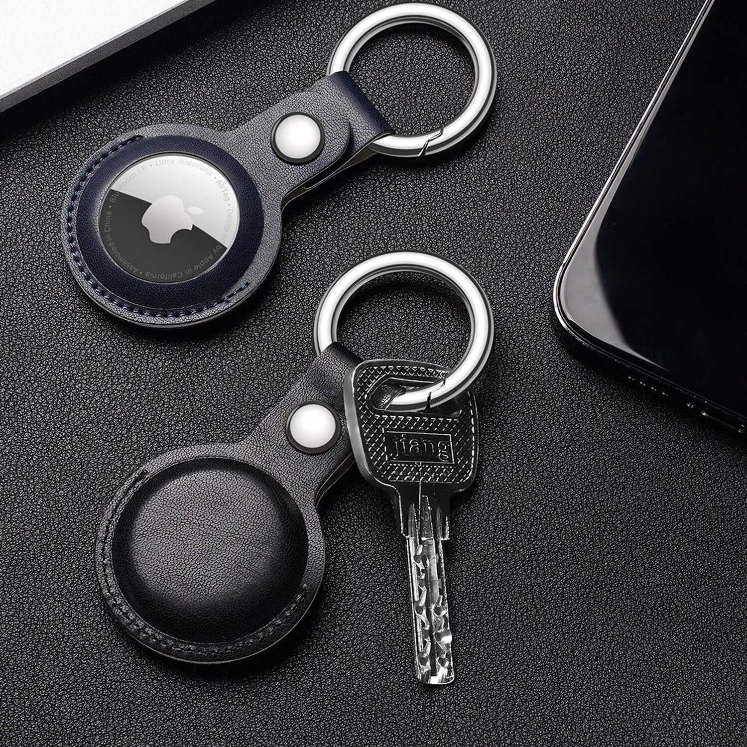 Zwei Schlüsselanhänger mit Schlüsseln. Einer hat ein schwarzes Lederetui mit einem Apple AirTag. Der andere hat einen Schlüssel.