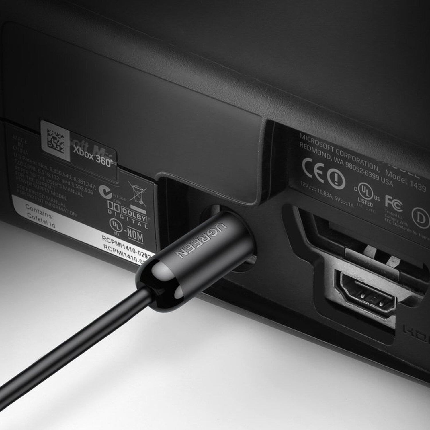 Czarny kabel wpięty z tyłu konsoli Xbox 360. Kabel ma zieloną etykietę UGREEN.