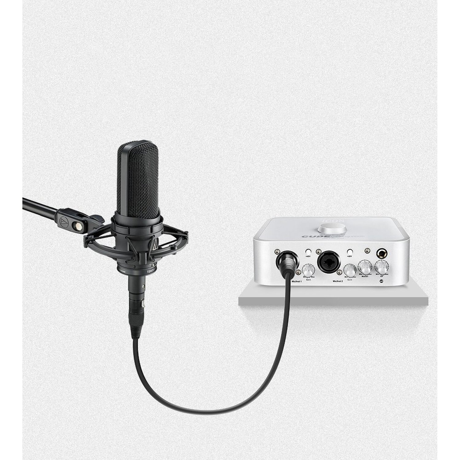 Ein schwarzes Mikrofon auf einem Ständer und ein silbernes Audiointerface, verbunden mit einem Kabel.