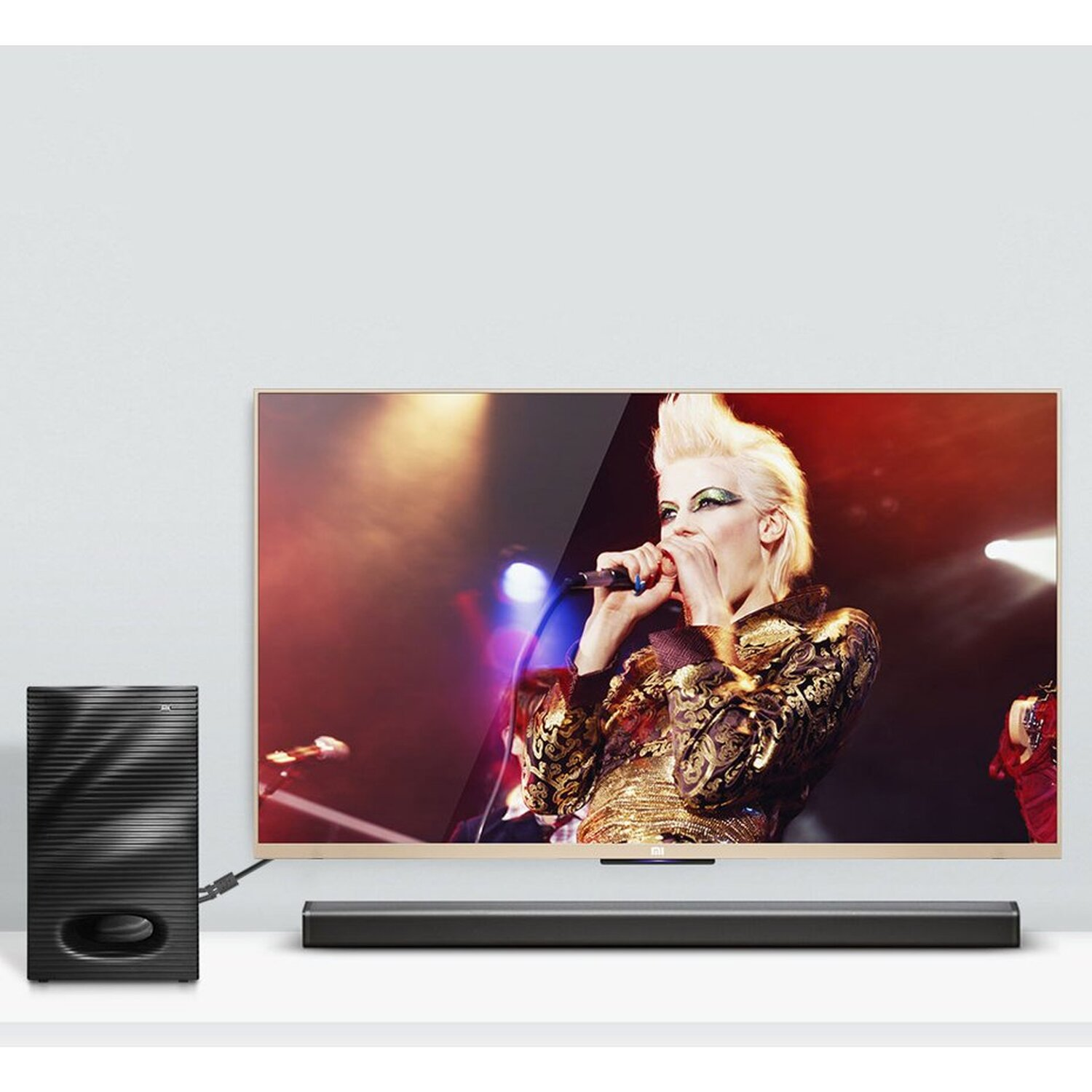 Telewizor wyświetla osobę śpiewającą do mikrofonu. Poniżej telewizora znajduje się soundbar i subwoofer.