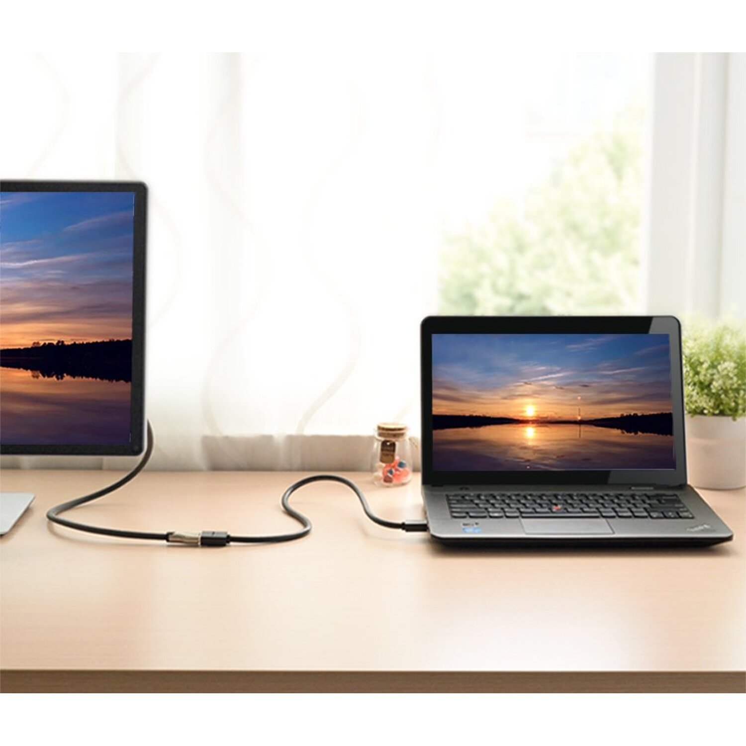 Laptop i monitor połączone kablem na drewnianym biurku.