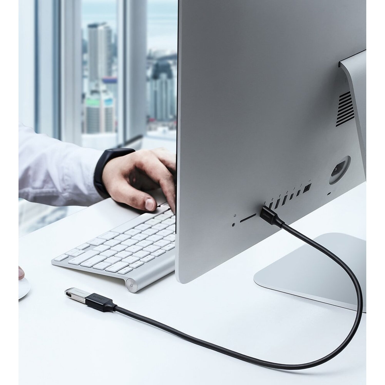 Een persoon die een laptop gebruikt die via een zwarte USB-kabel is aangesloten op een monitor. De monitor staat op de achtergrond.