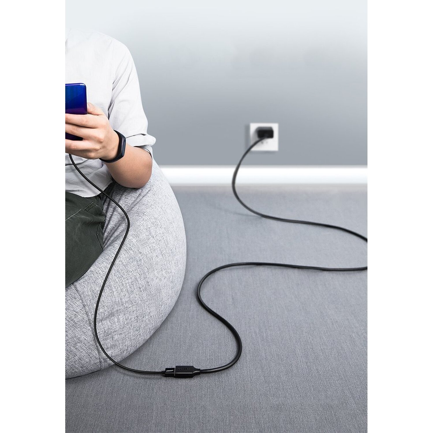 Persoon zit met een telefoon verbonden met een zwarte oplaadkabel.